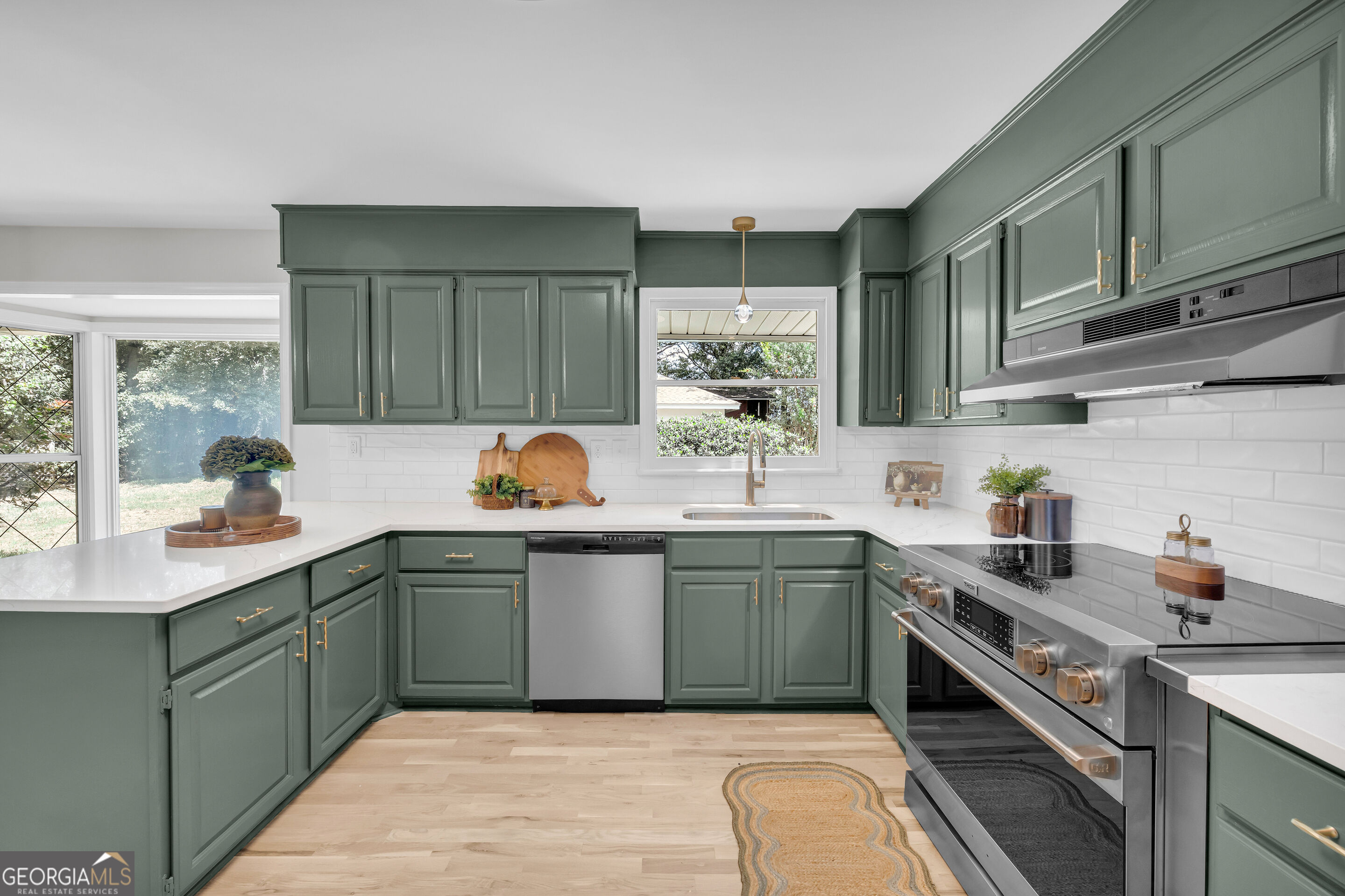 Kitchen with sage-green cabinets, white counters, stainless-steel appliances, and brass hardware.