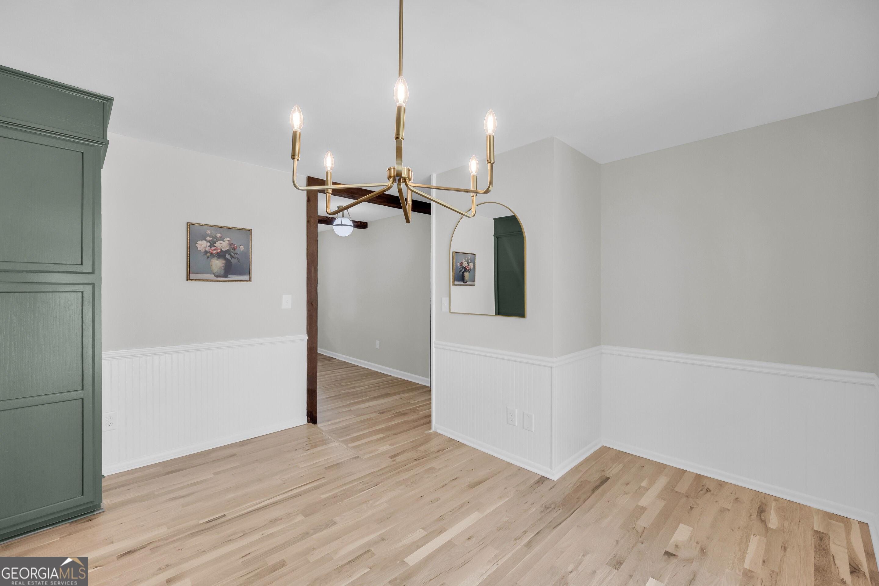 Dining area with light wood floors, white wainscoting, a brass chandelier, and dark green built-in cabinetry.