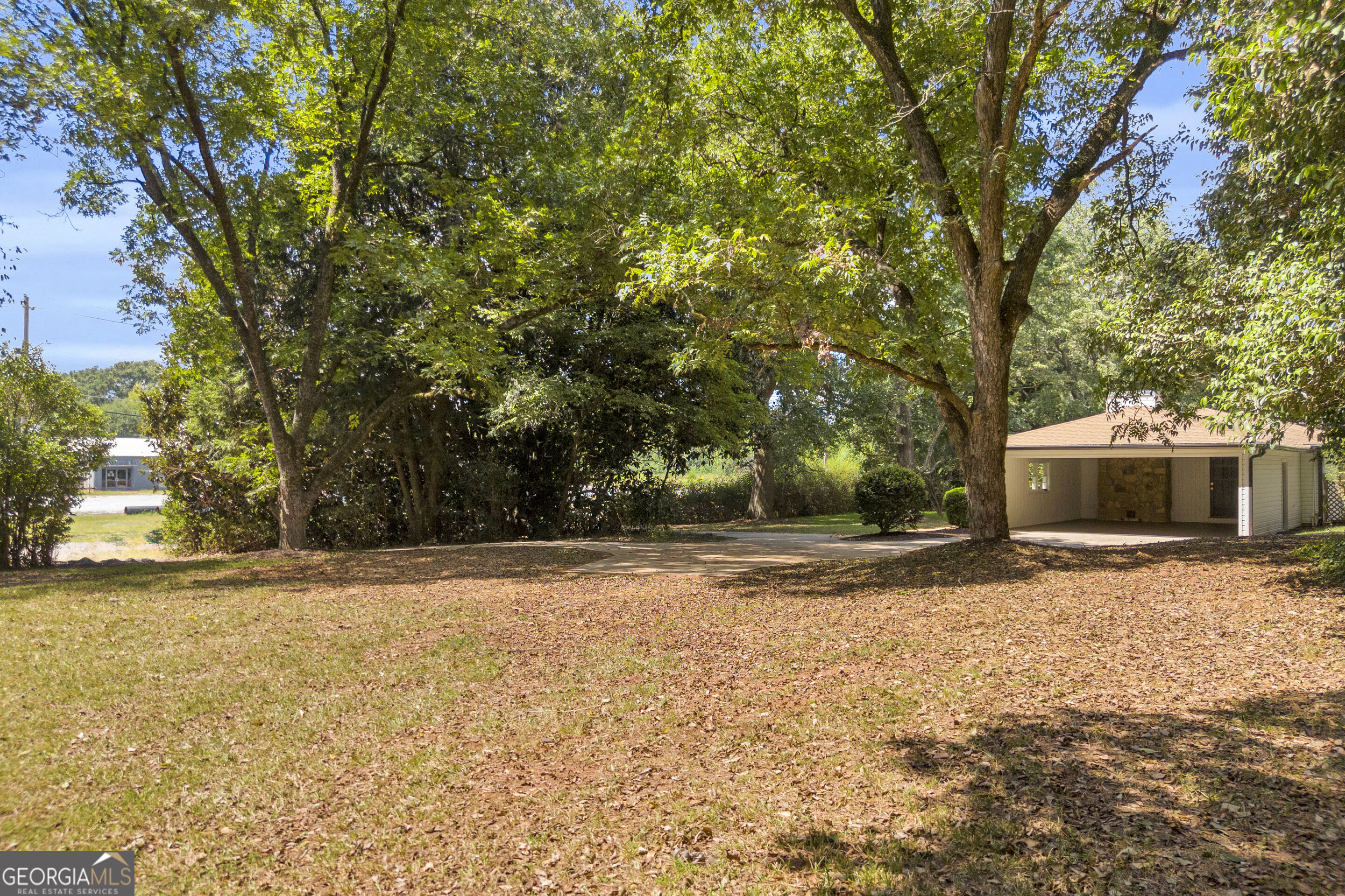 Yard with mature shade trees, a paved driveway, and a detached open-sided carport.