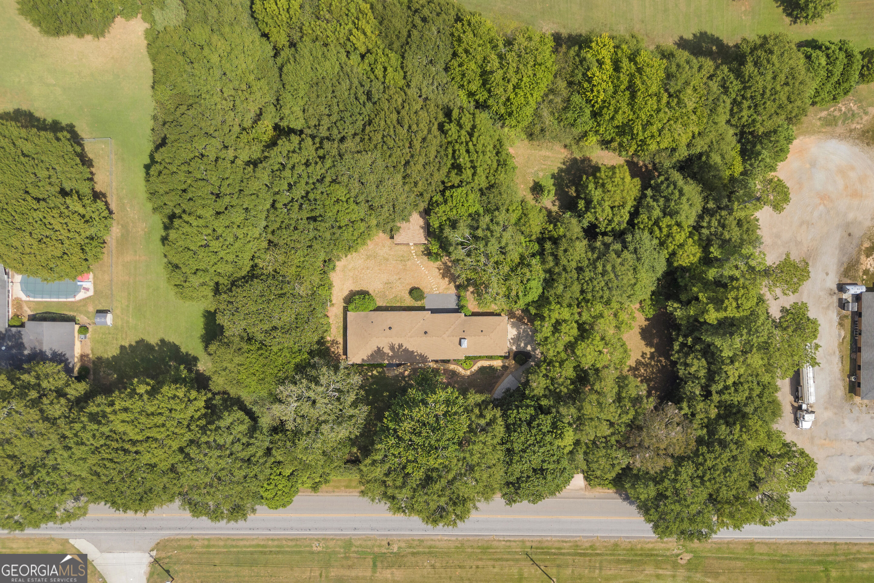 Aerial view of a tan-roofed home nestled among dense trees beside a paved road.