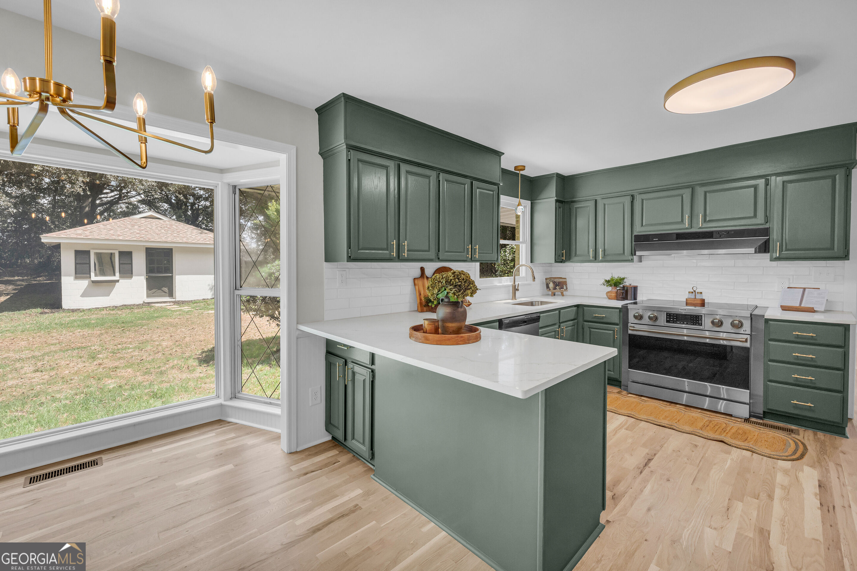 Renovated kitchen with green cabinets, a large white island, and windows overlooking the yard.