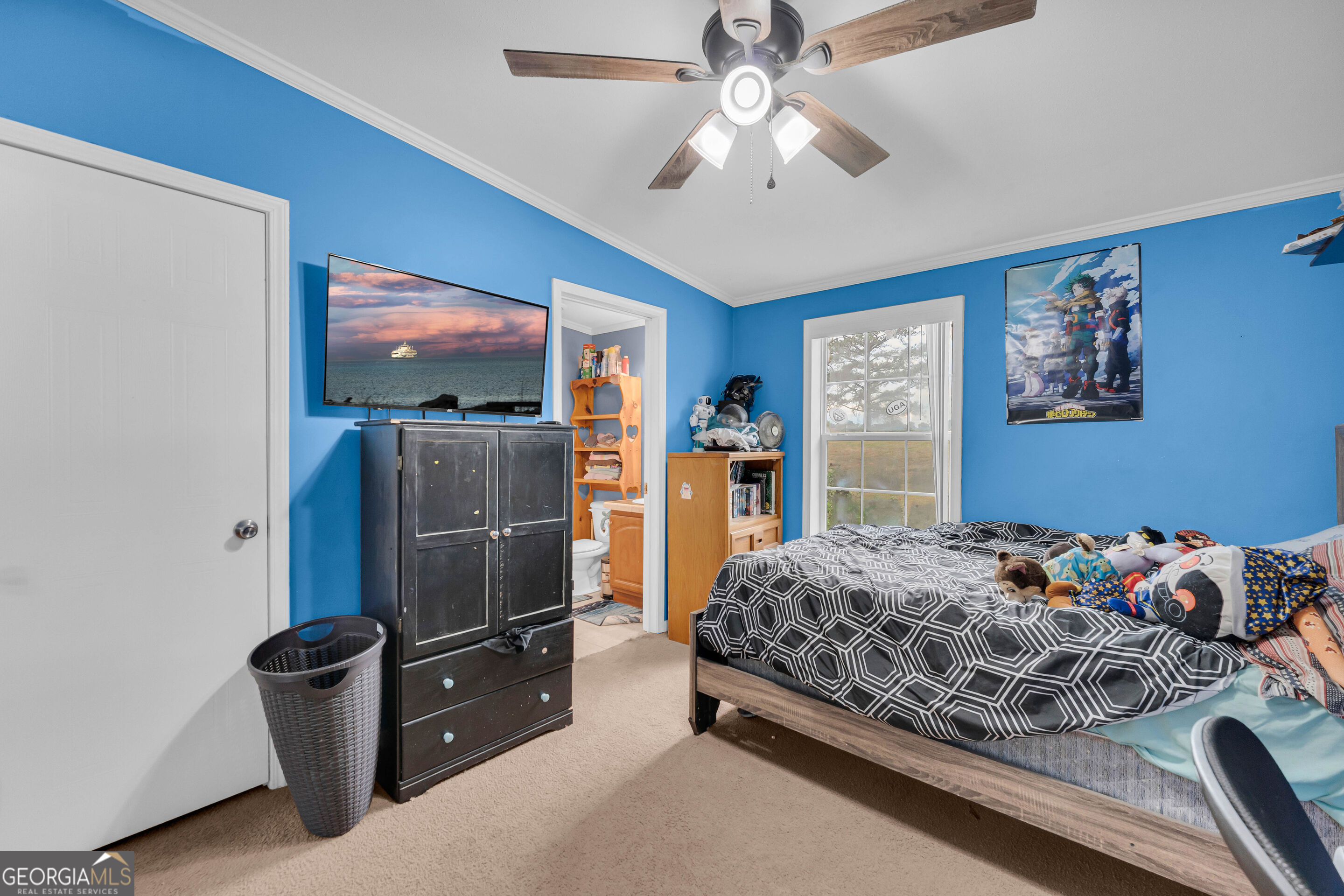 Bedroom with bright blue walls, geometric bedding, a ceiling fan, and an adjoining bathroom doorway.