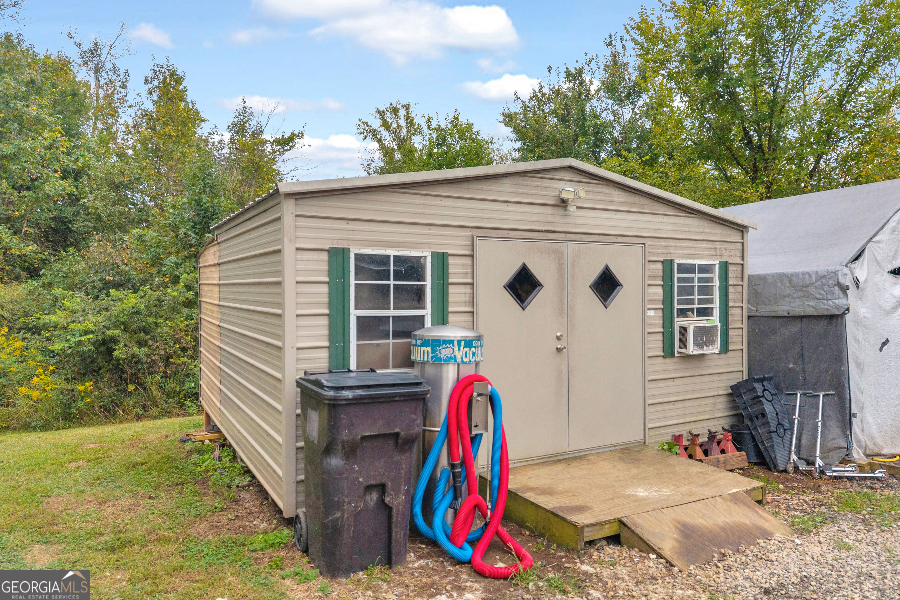 Beige metal outbuilding with green shutters, double doors, and a wooden ramp.
