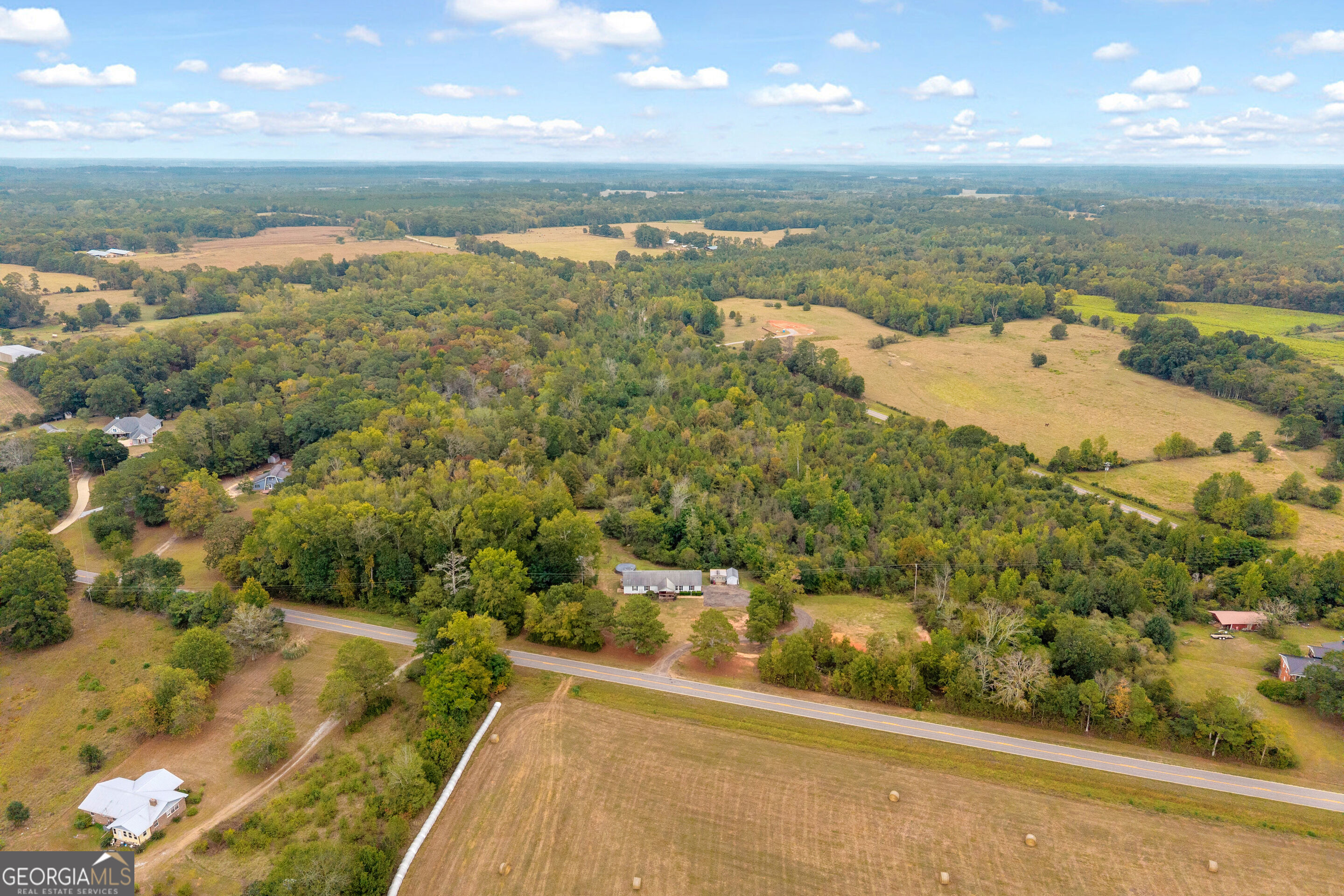Aerial view of wooded rural acreage and open fields with scattered homes beside a road.