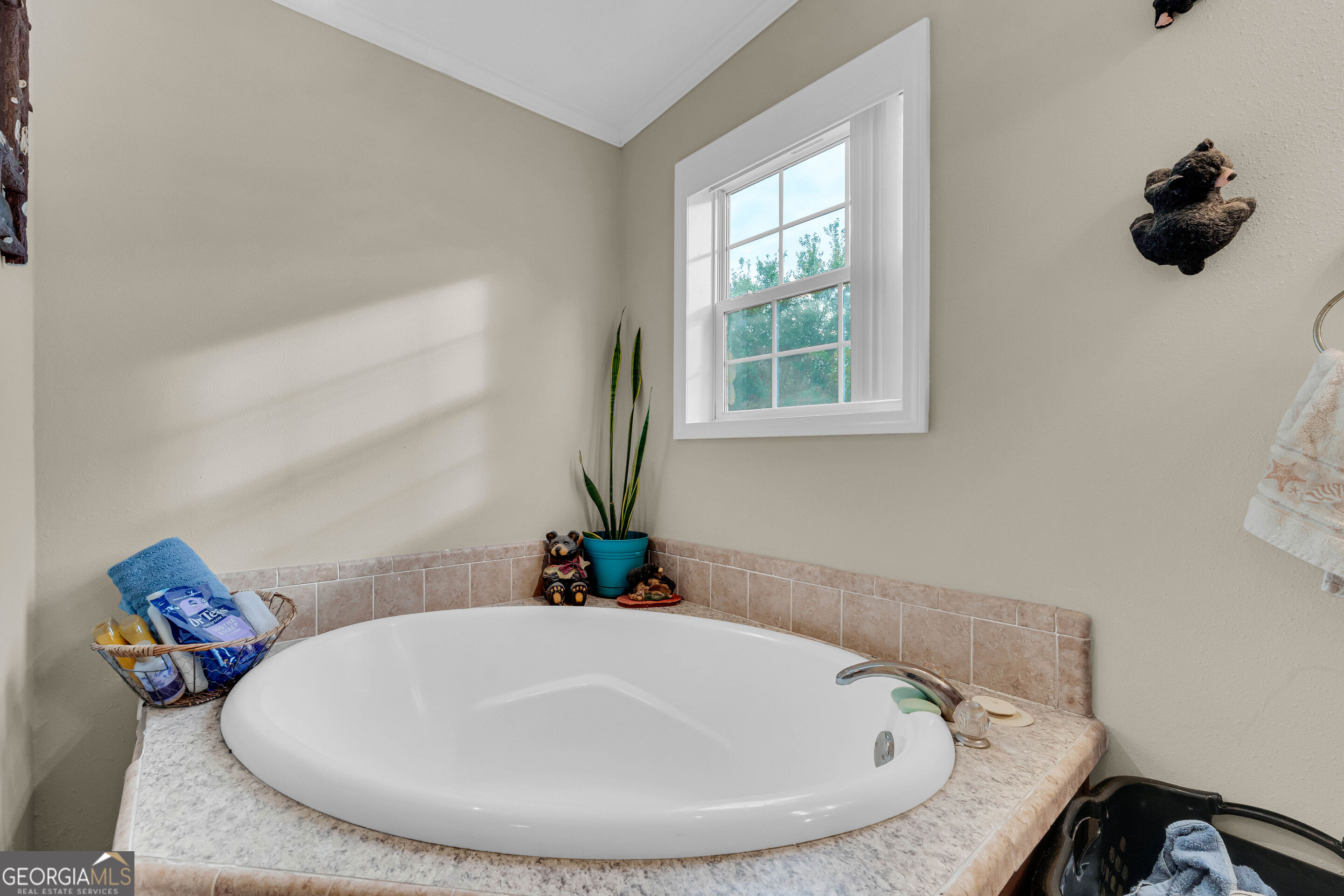 Oval soaking tub beneath a window, with tiled surround and a potted plant.