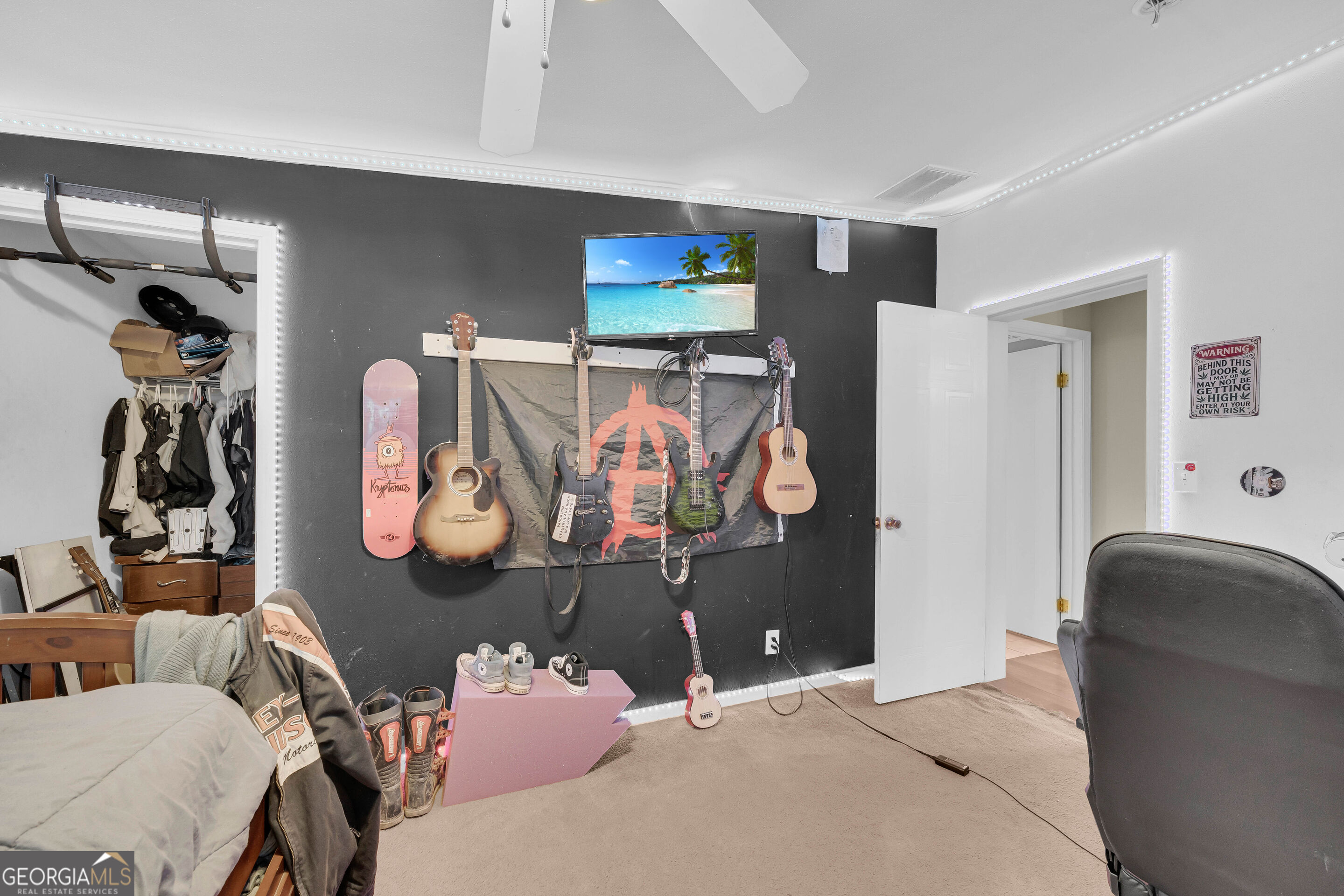Bedroom with guitars and a skateboard displayed on a black wall, outlined by LED lights.