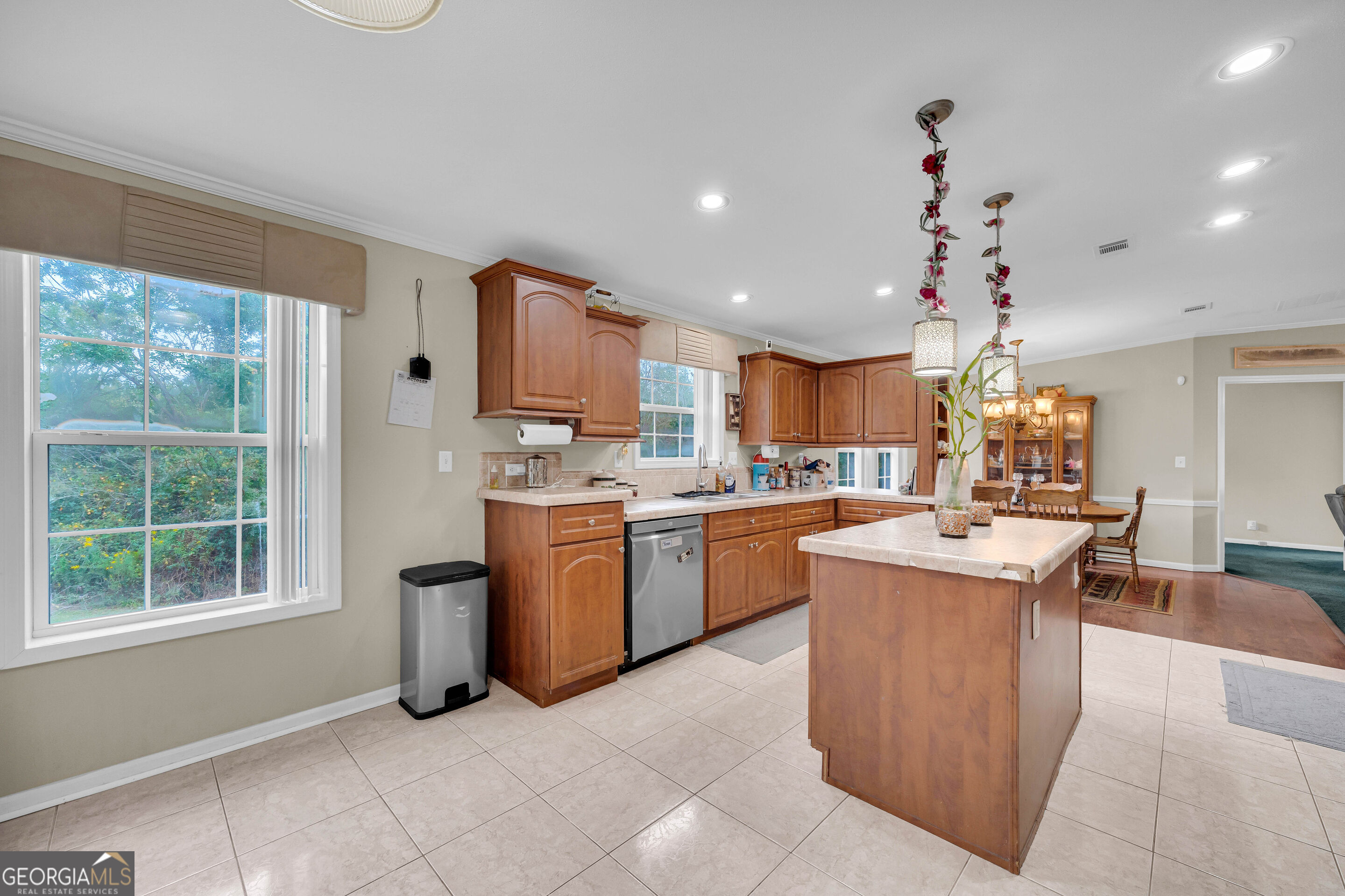 Kitchen with wood cabinets, a large island, tiled floors, and windows overlooking greenery.