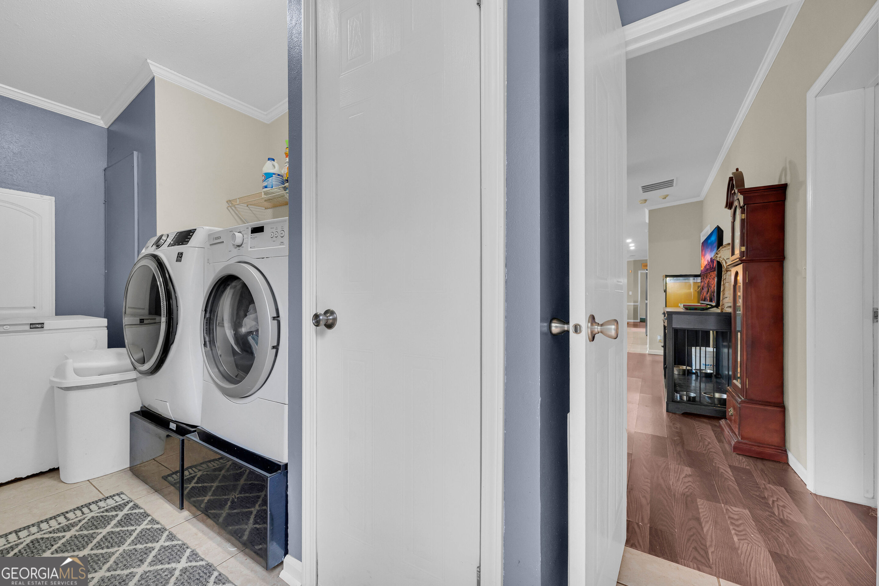 Laundry room with front-loading washer and dryer beside a doorway to a furnished hallway.