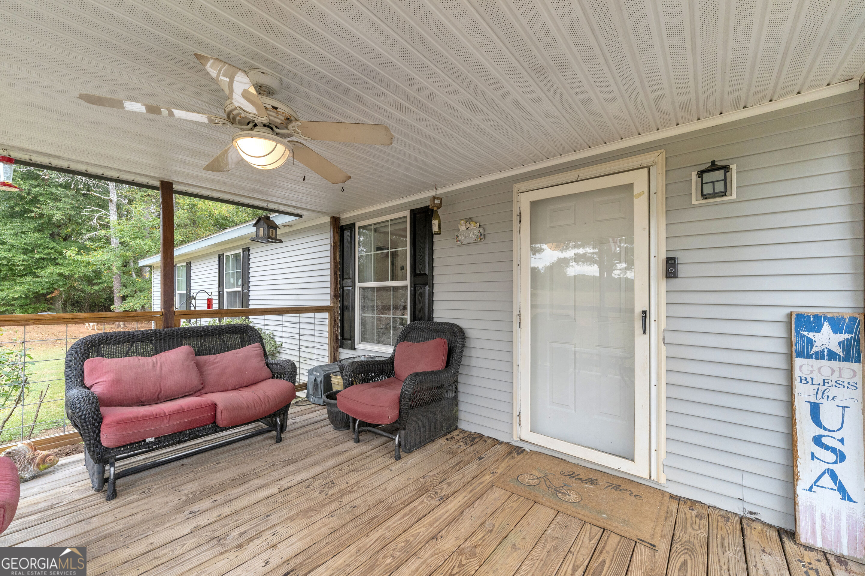 Covered front porch with wicker seating, rose cushions, and a weathered wood deck.