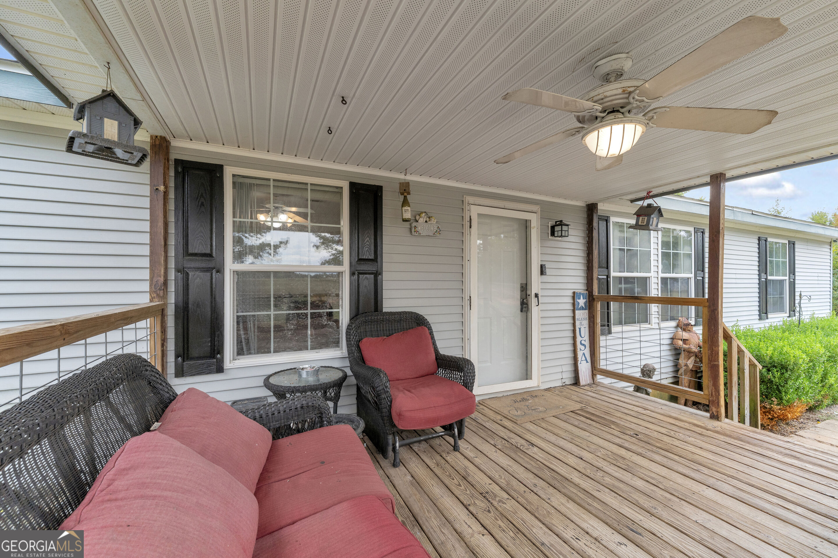 Covered wooden porch with wicker seating, red cushions, and a ceiling fan.