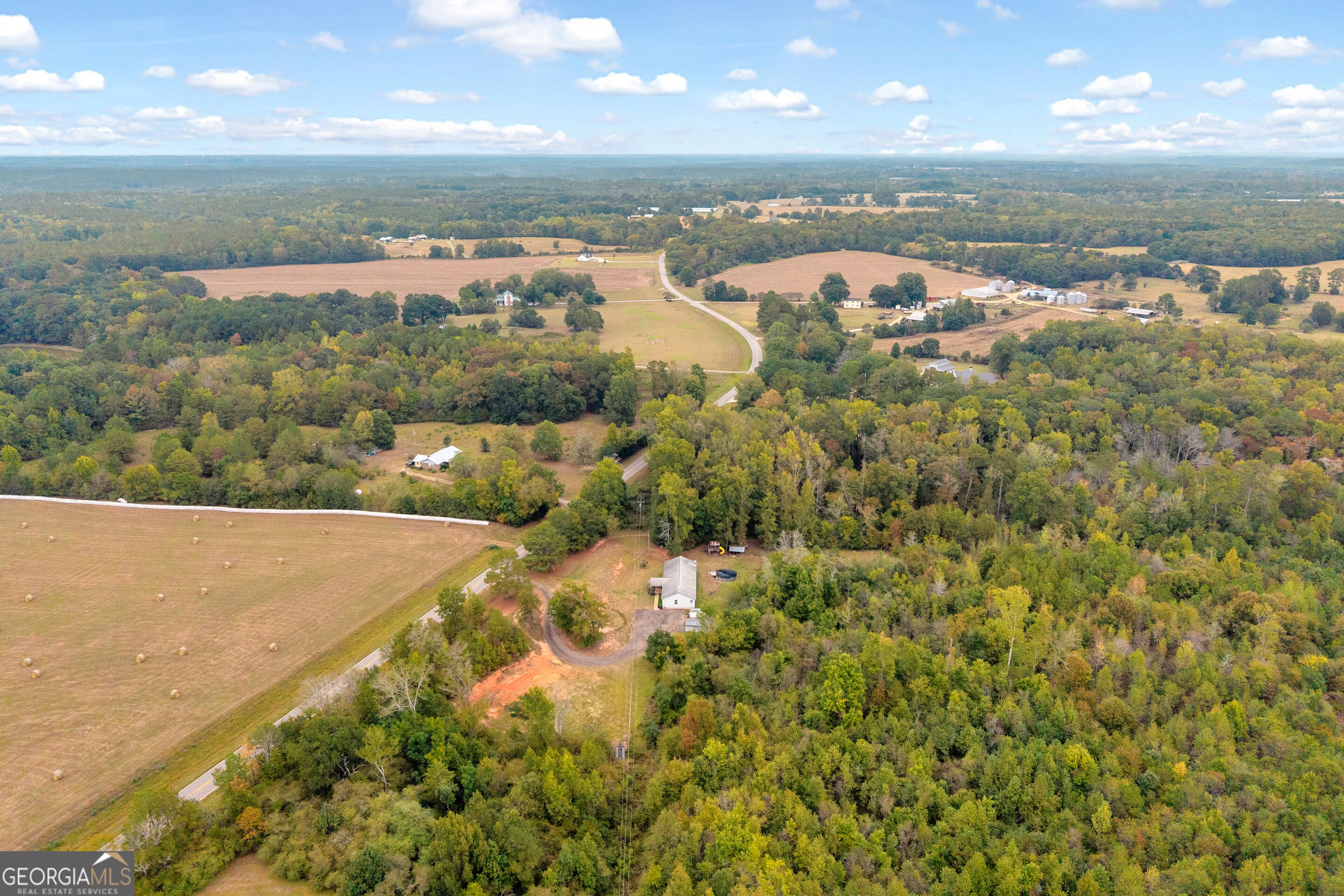 Aerial view of a rural home amid autumn woodland, open hay fields, and winding country roads.