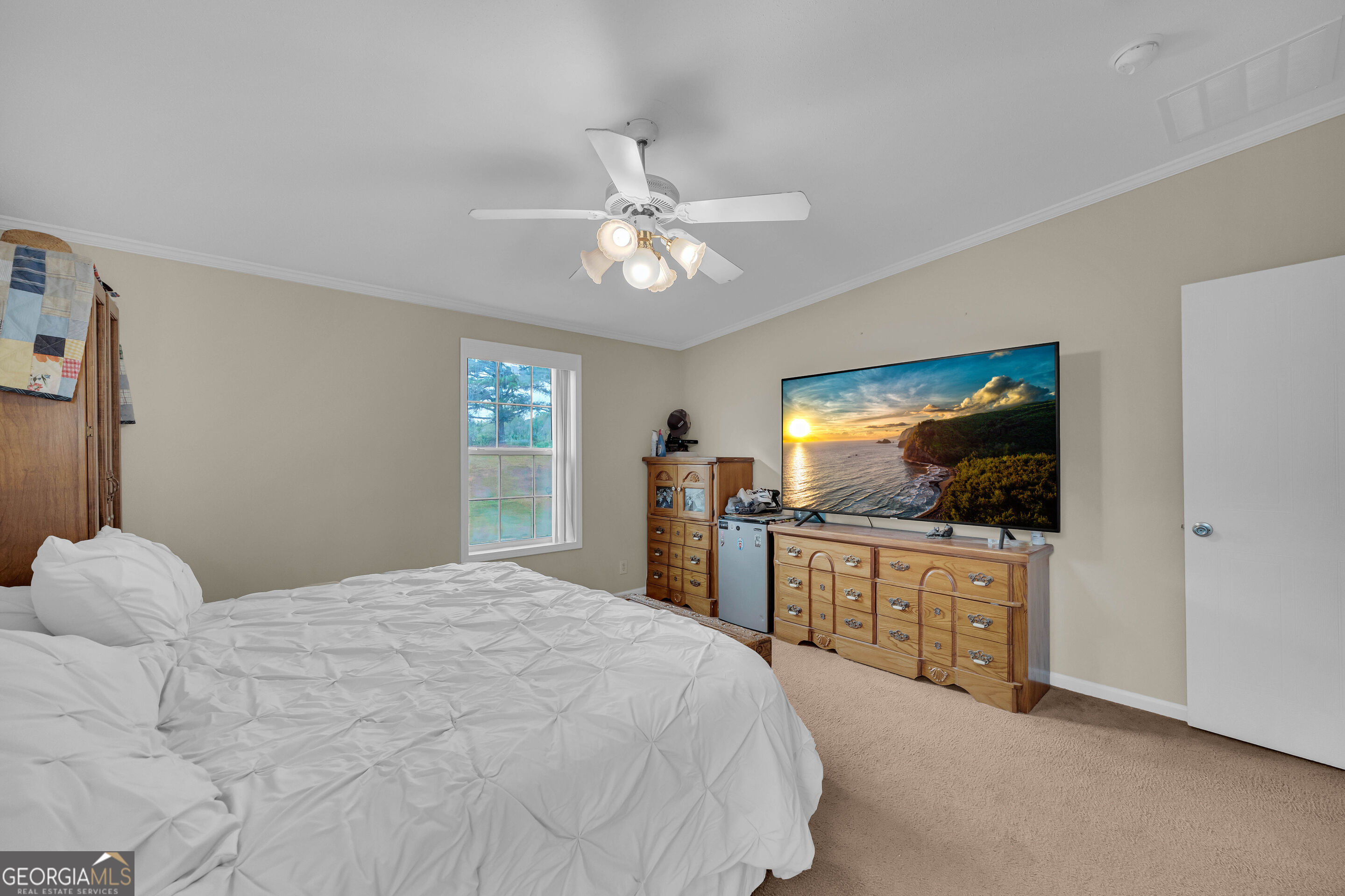 Bedroom with a large white bed, wooden dressers, and a television displaying a coastal sunset.
