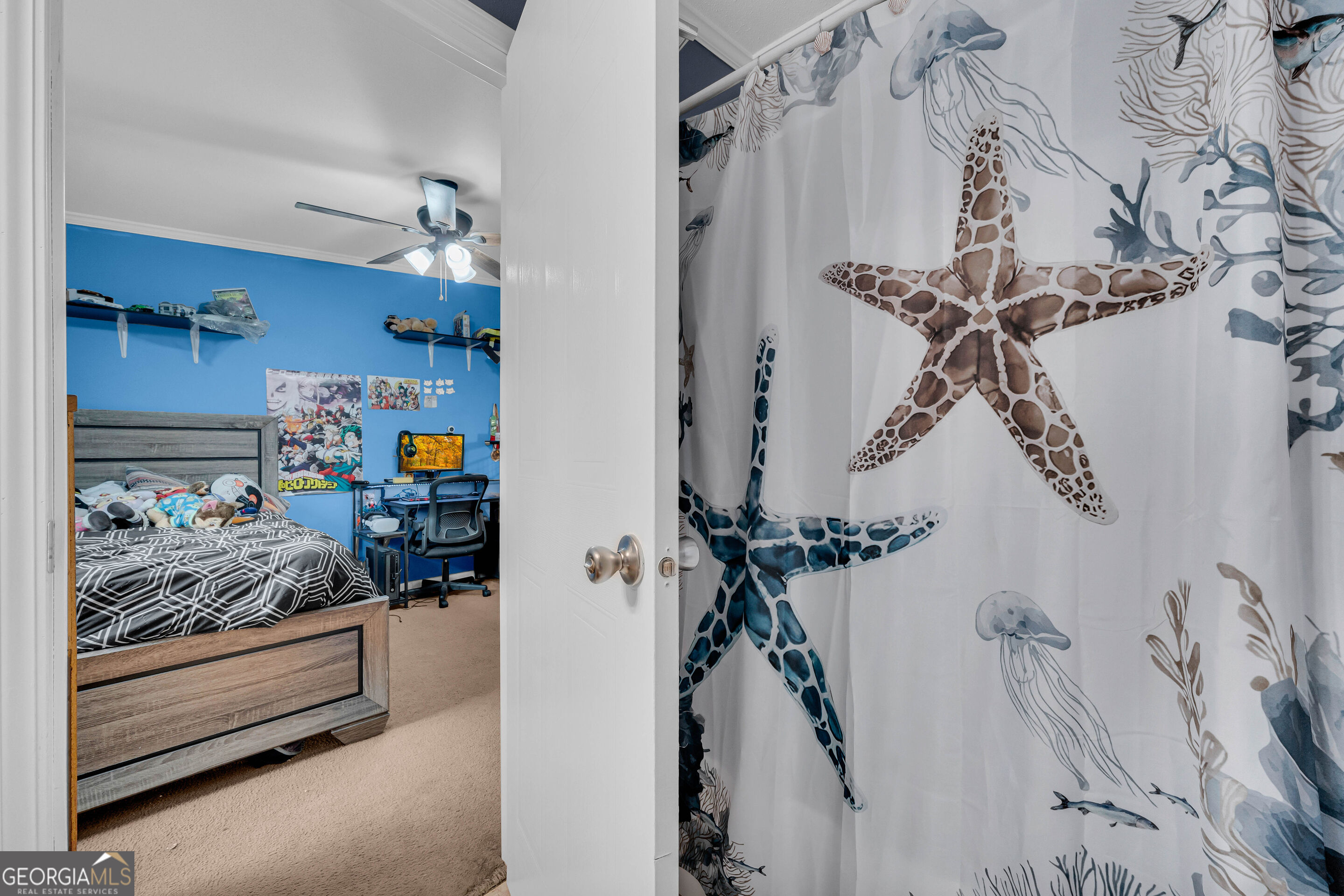 Bedroom with bright blue walls, a bed, computer desk, and marine-themed shower curtain.