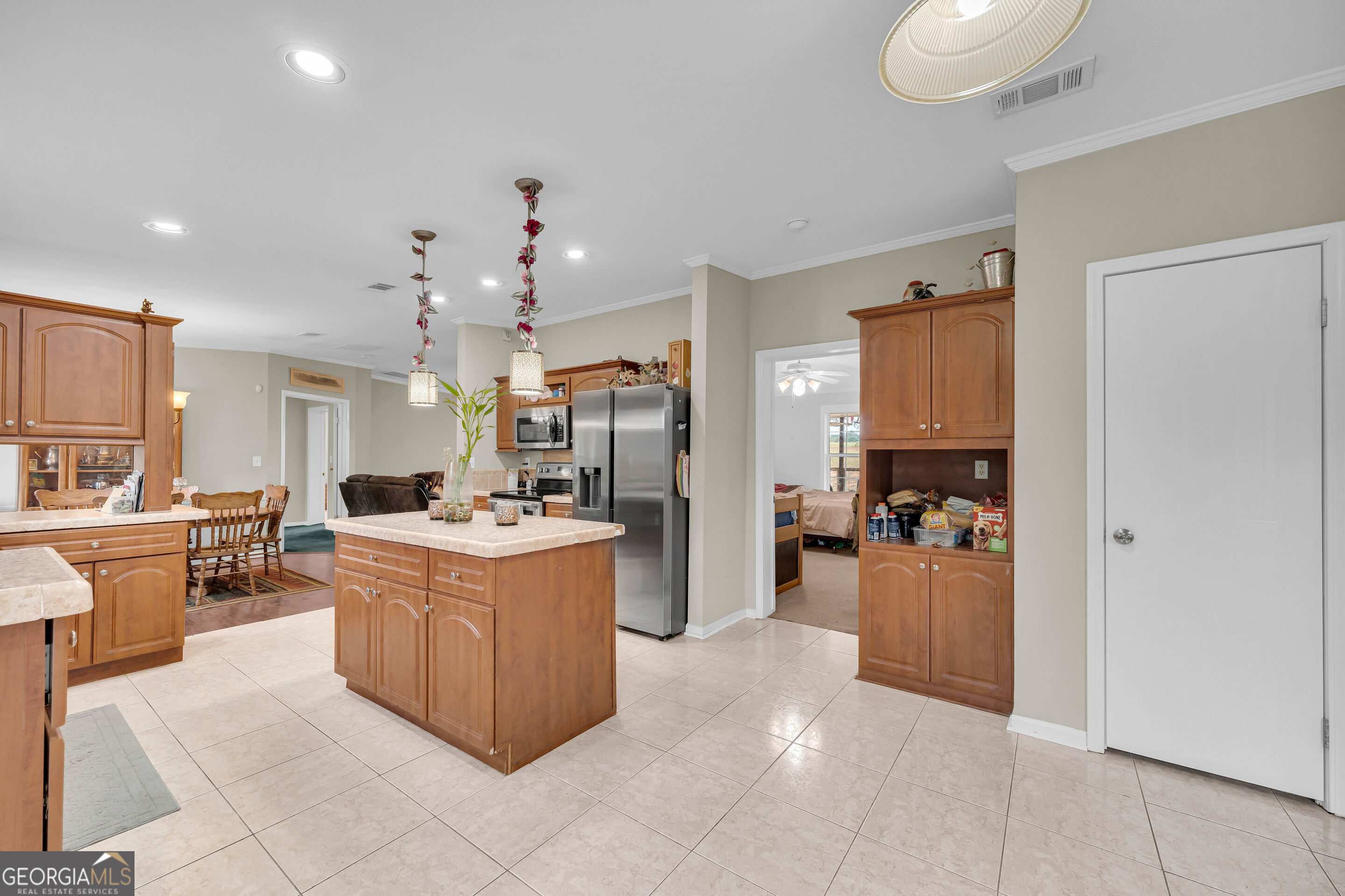 Kitchen with wood cabinetry, central island, stainless steel appliances, and large tile floor.