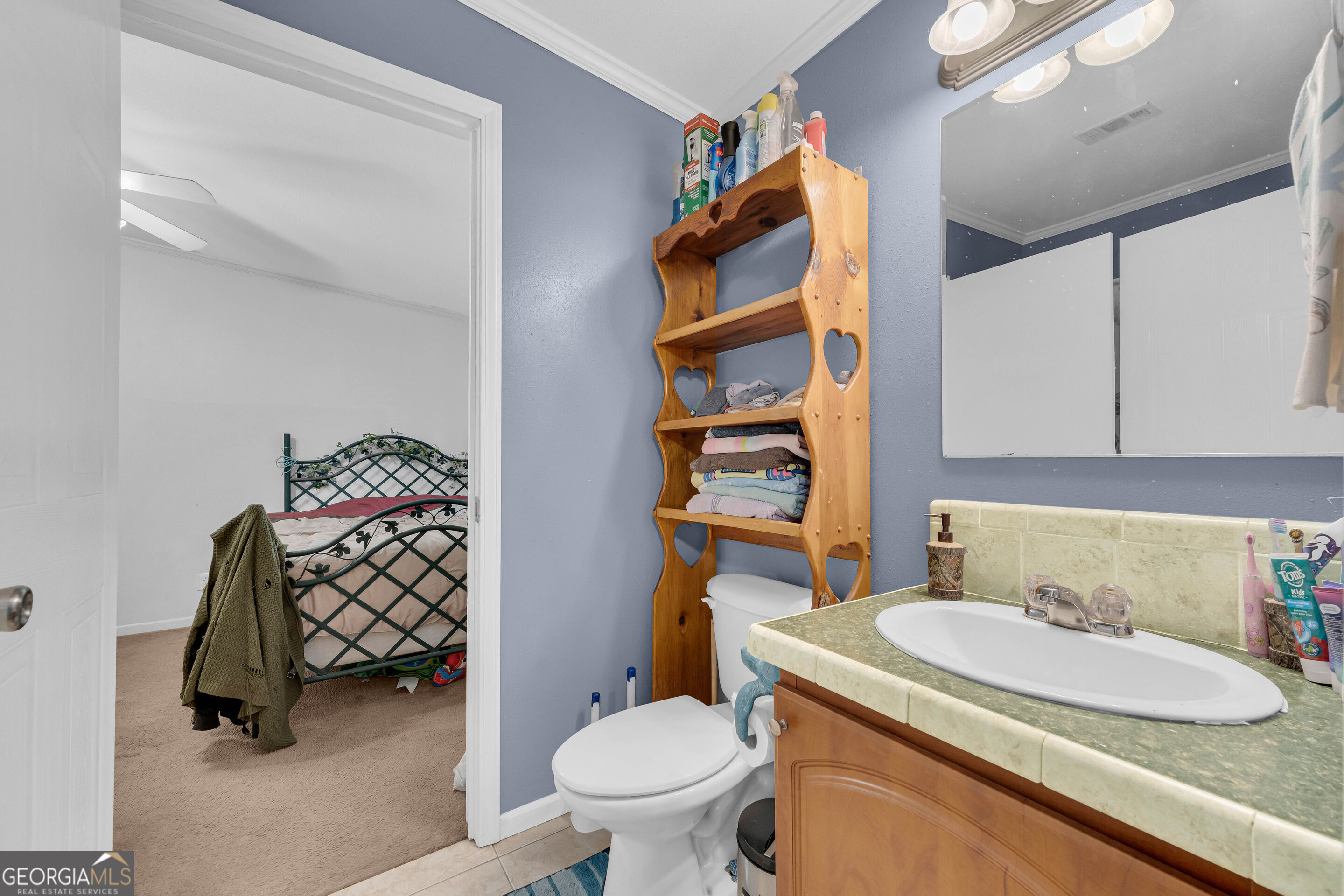 Bathroom with a green countertop, white sink, wooden vanity, and open doorway to a bedroom.