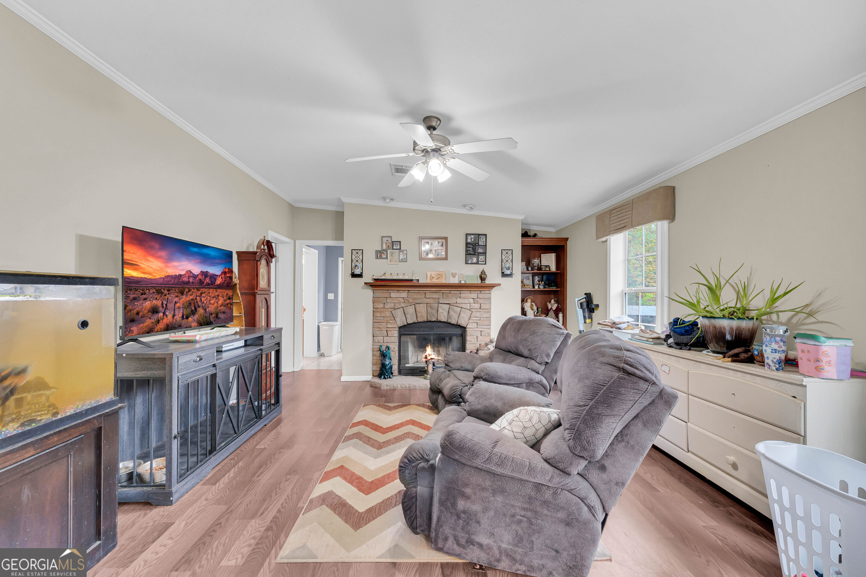 Living room with a stone fireplace, gray reclining sofas, and a television on a console.