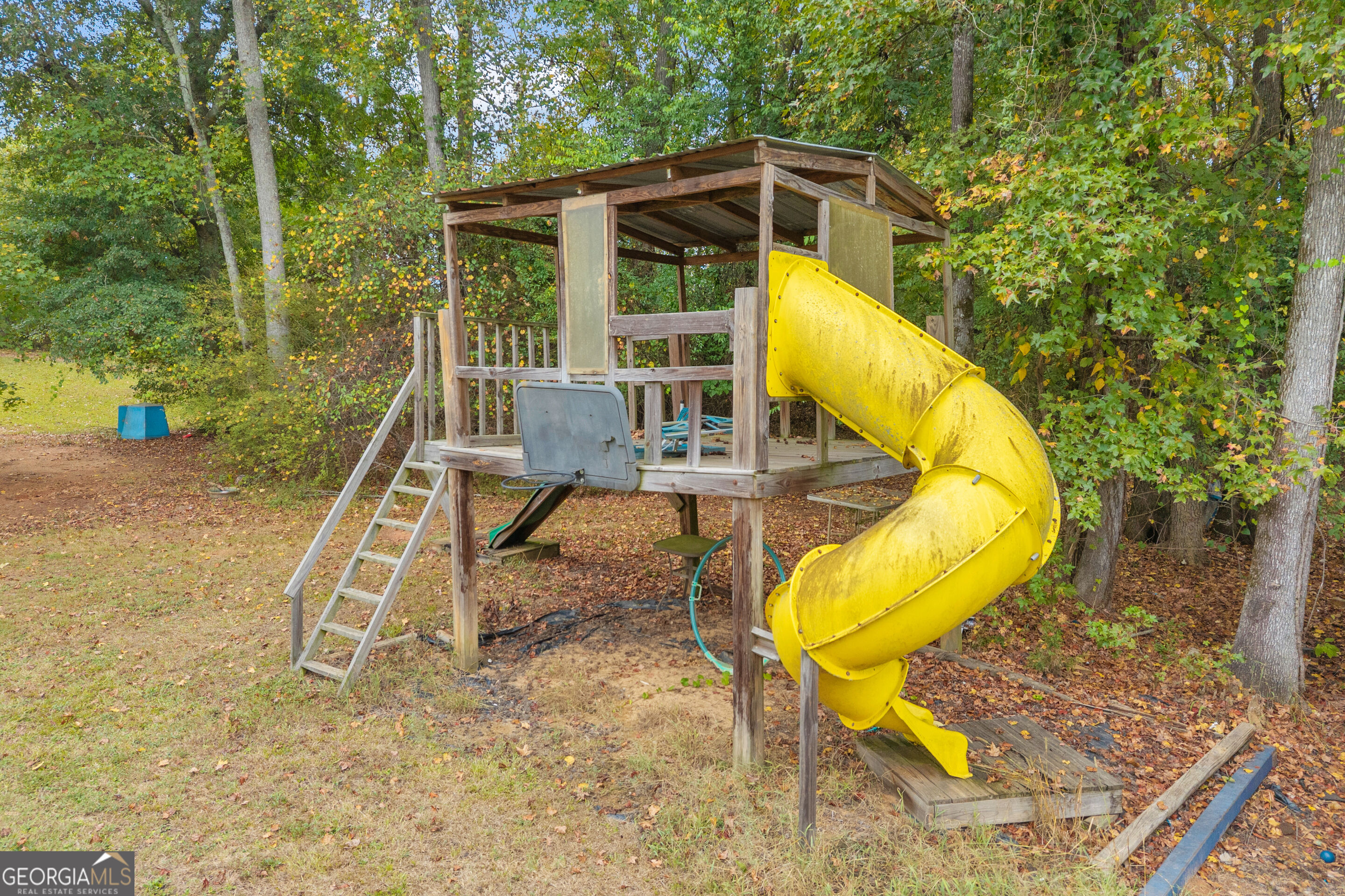 Backyard playset with a large yellow spiral slide beneath the trees.
