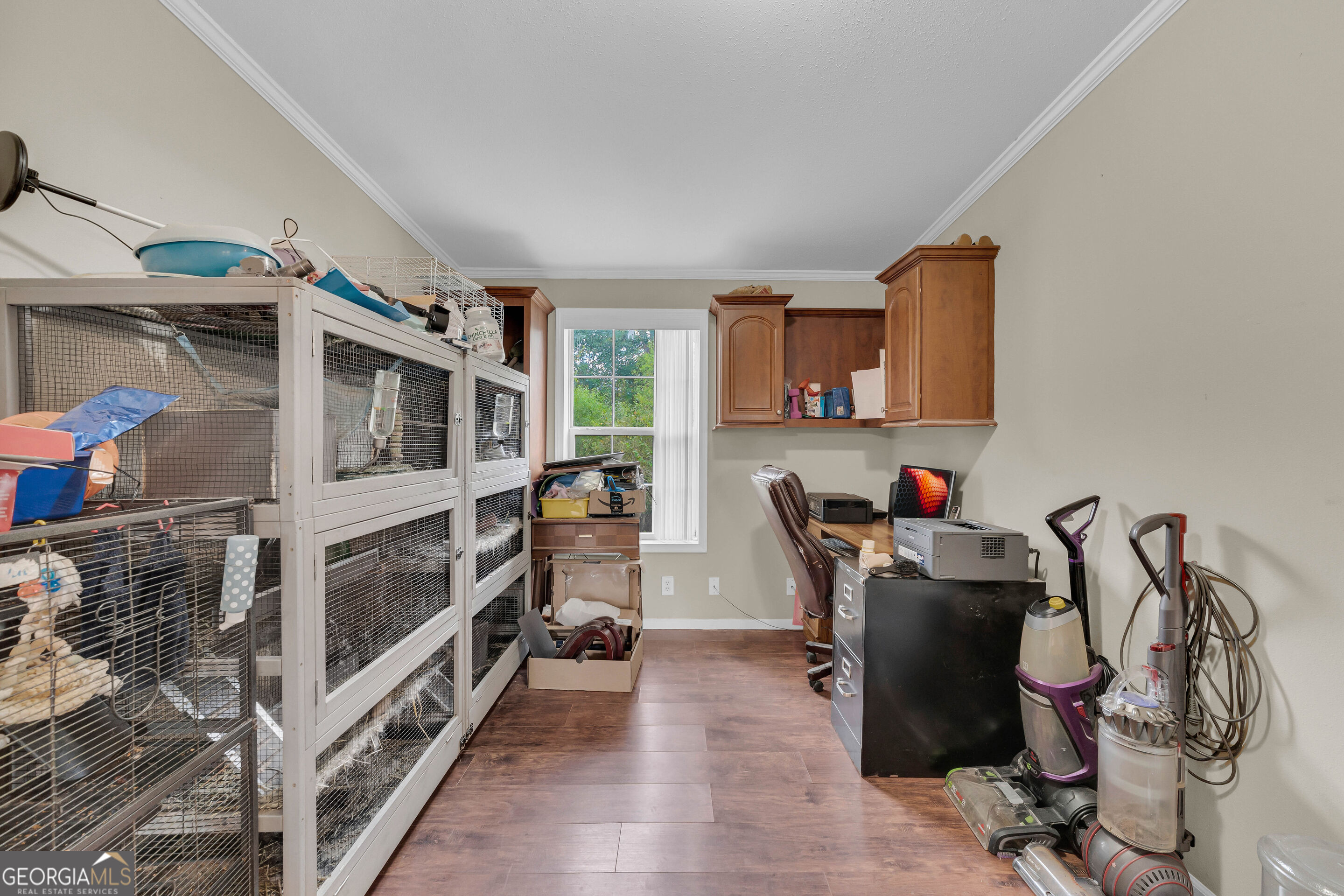 Utility room with large wire animal enclosures, wooden cabinets, office equipment, and cleaning appliances.