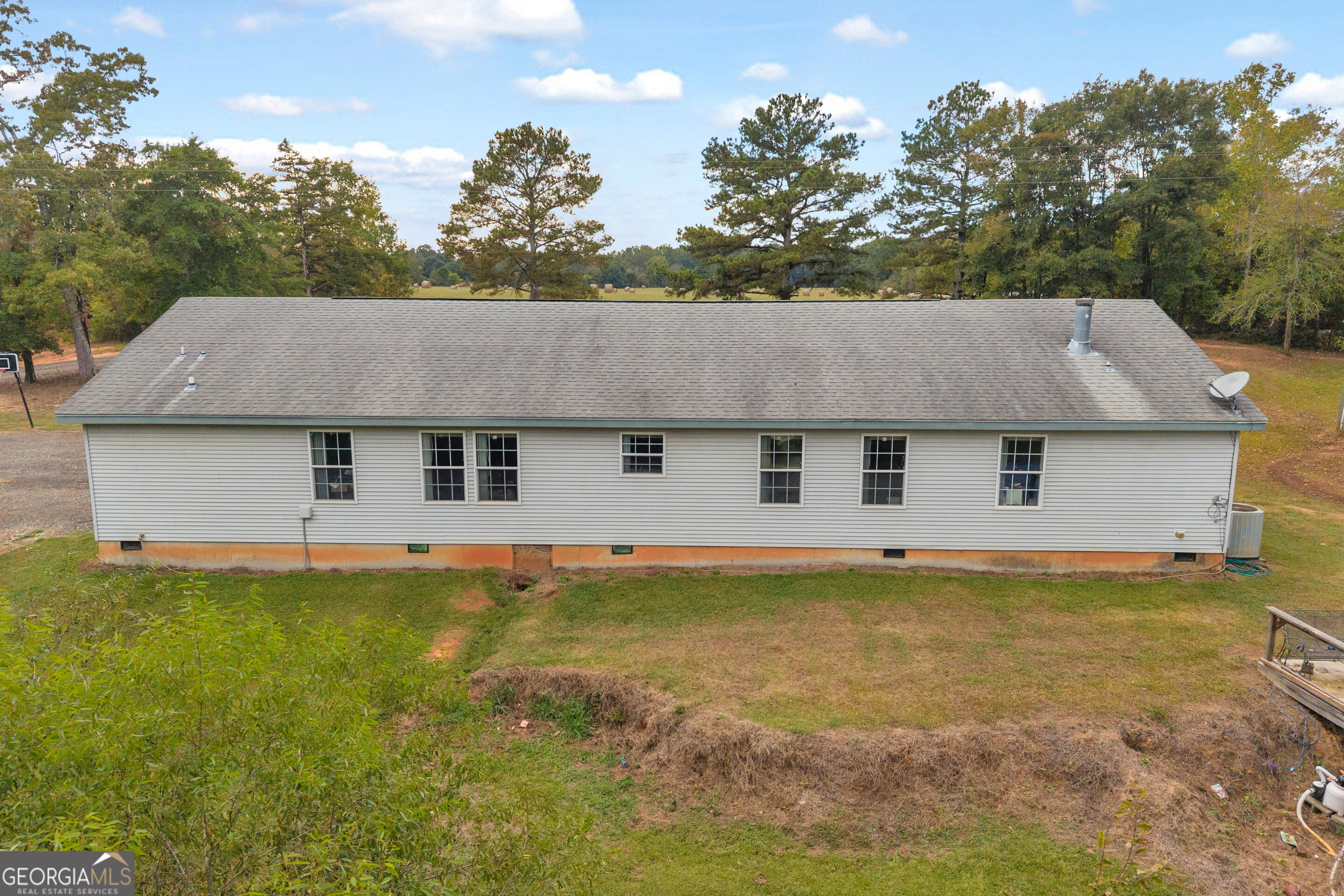 Rear of a long, single-story home with light siding, a broad roof, and a grassy yard.