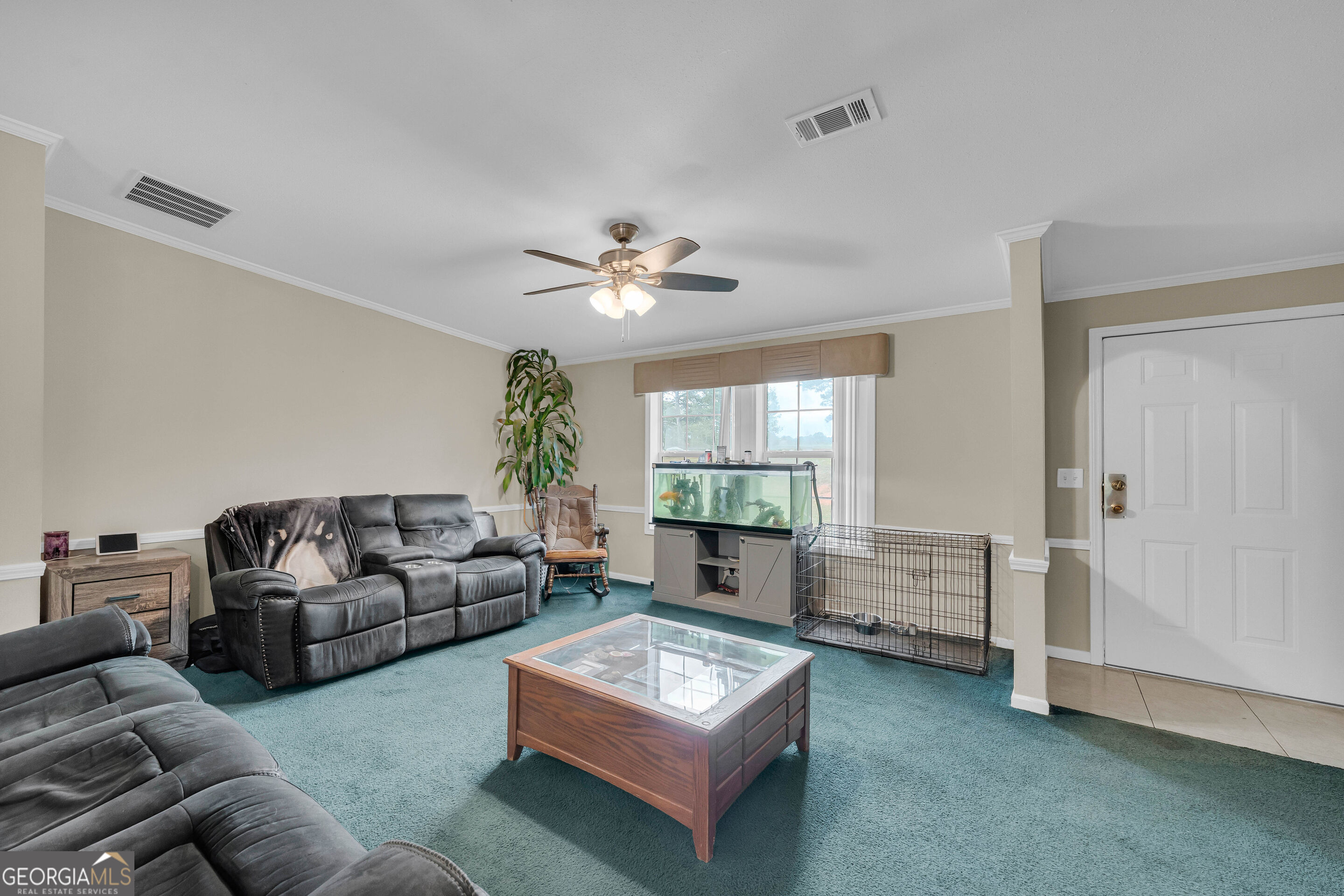 Furnished living room with teal carpet, gray reclining sofas, an aquarium, and a metal dog crate.