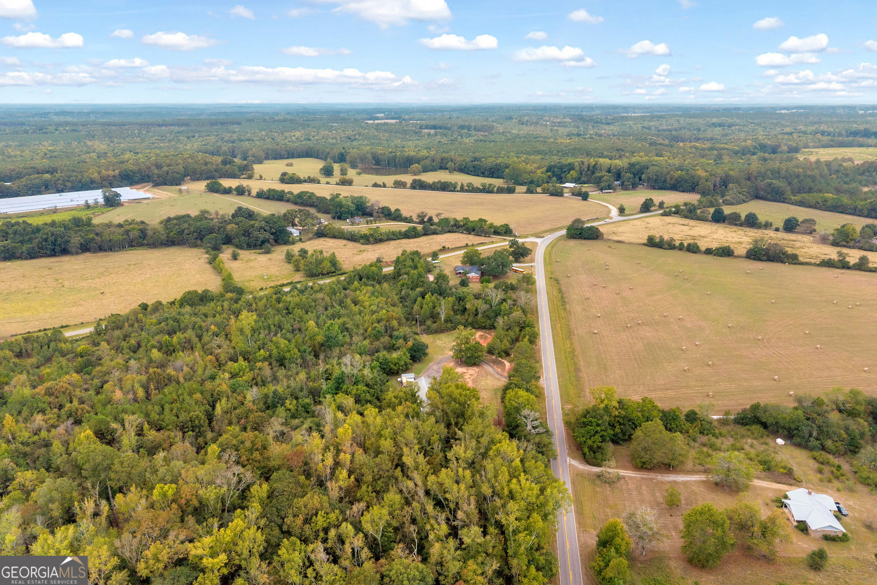Aerial view of wooded rural land, open fields, and a winding road beside scattered homes.
