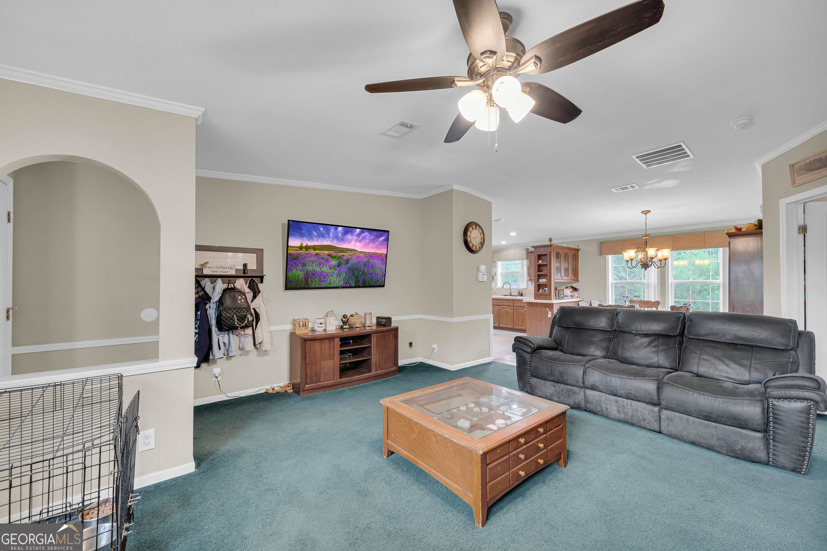 Living room with teal carpet, gray leather sofa, wooden coffee table, and an open view into the kitchen.