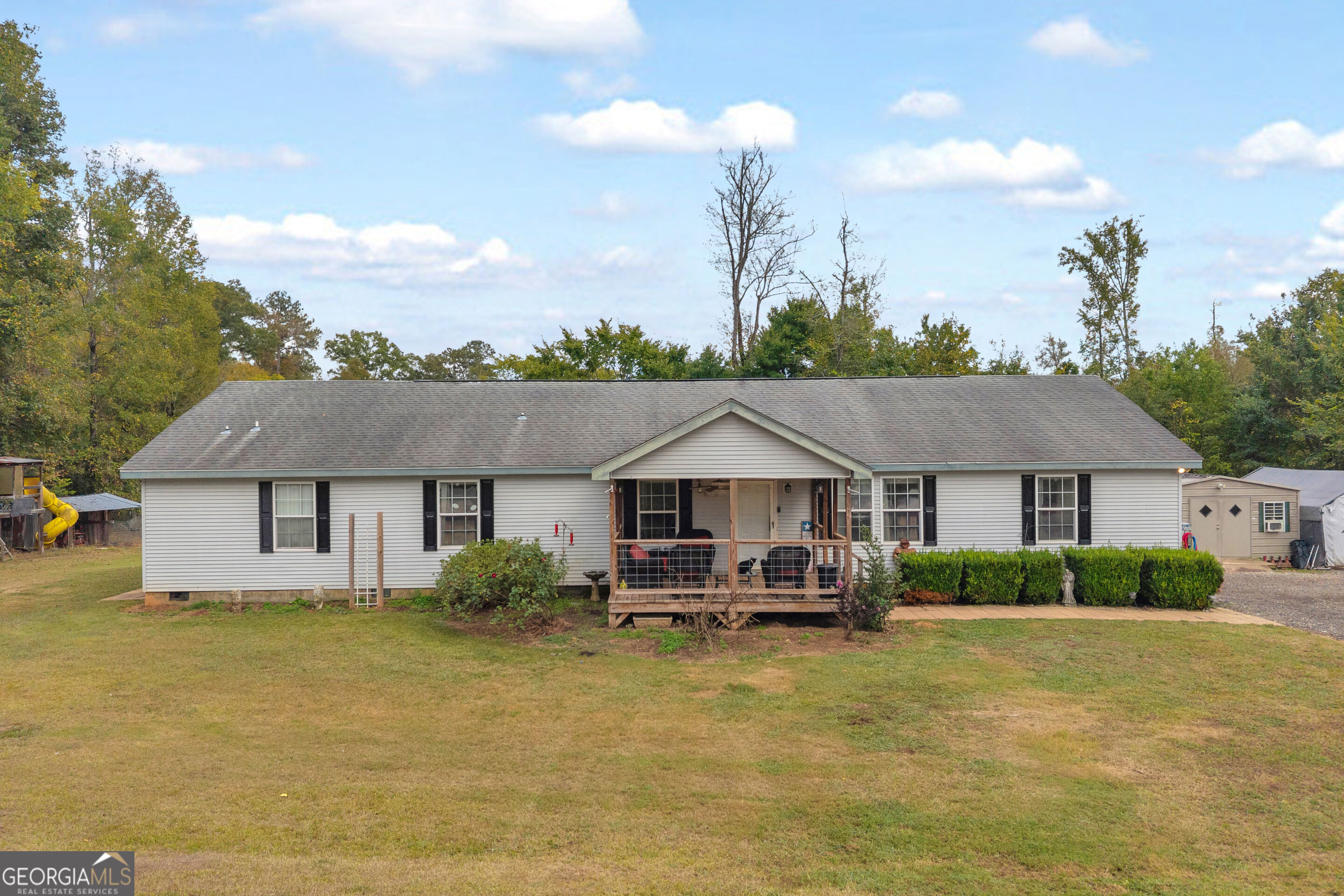 Single-story home with light siding, black shutters, a covered porch, and a broad front lawn.
