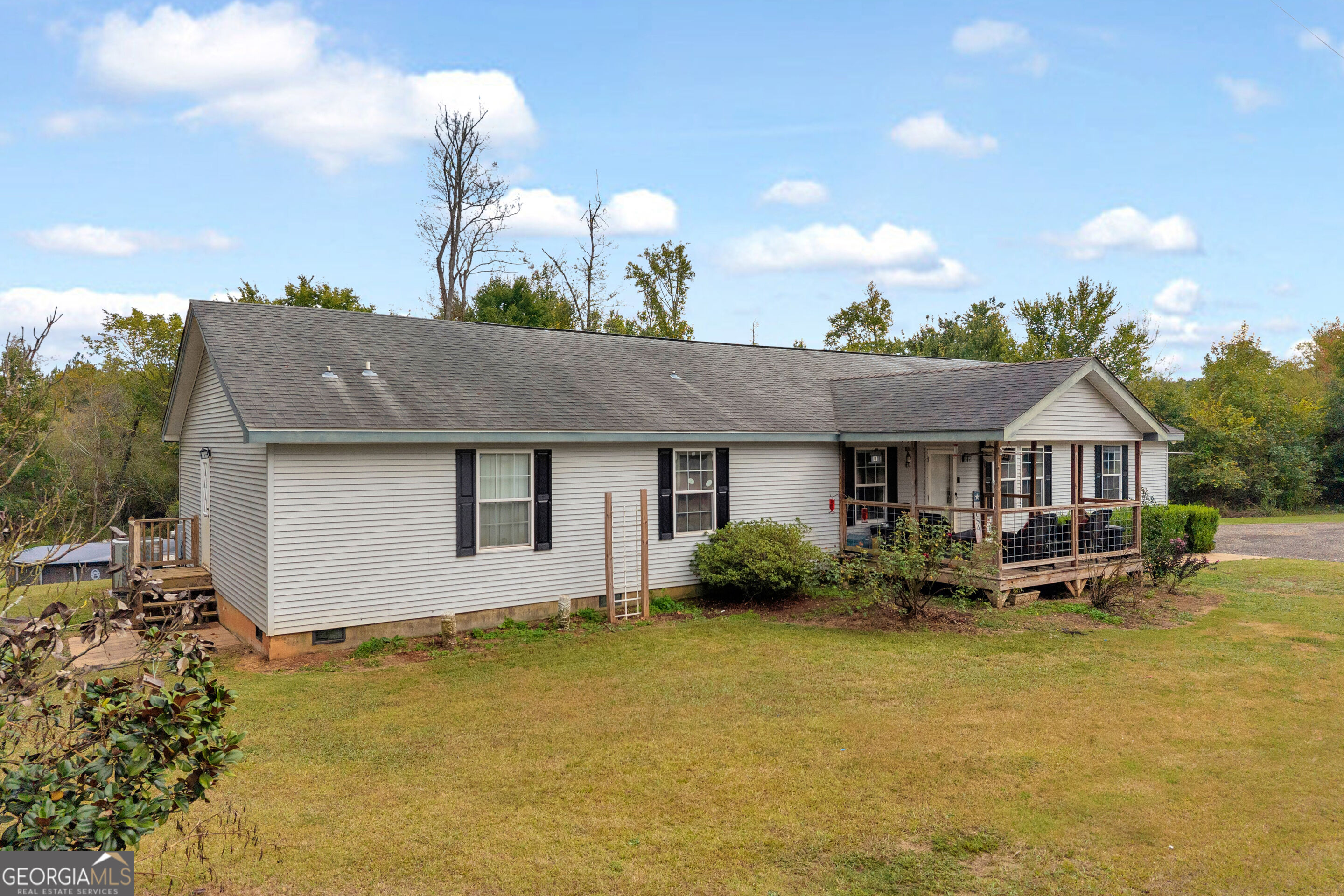 Single-story home with light siding, a covered wooden porch, and a broad lawn.