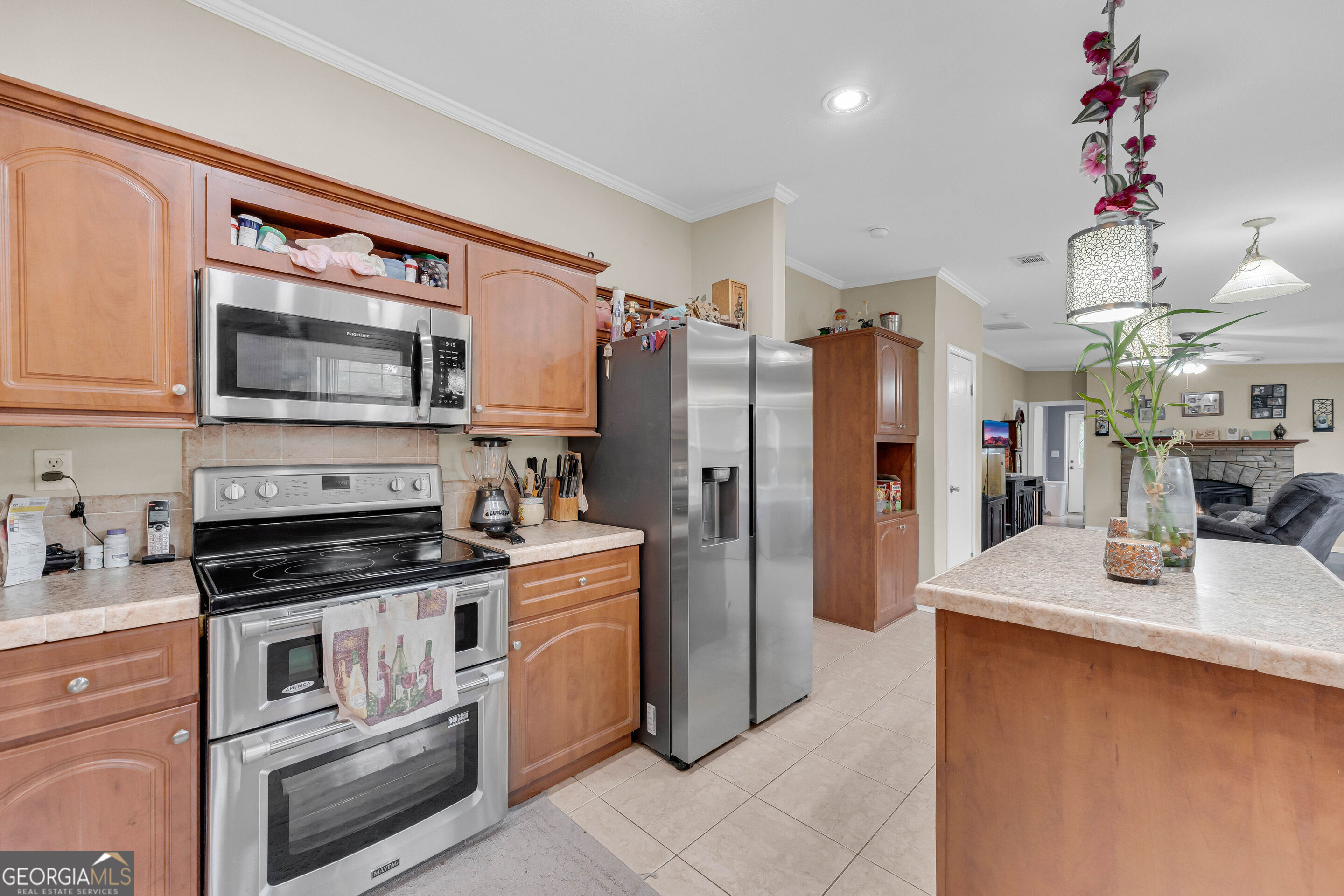 Kitchen with warm wood cabinets, stainless steel appliances, and a tiled island with a vase.