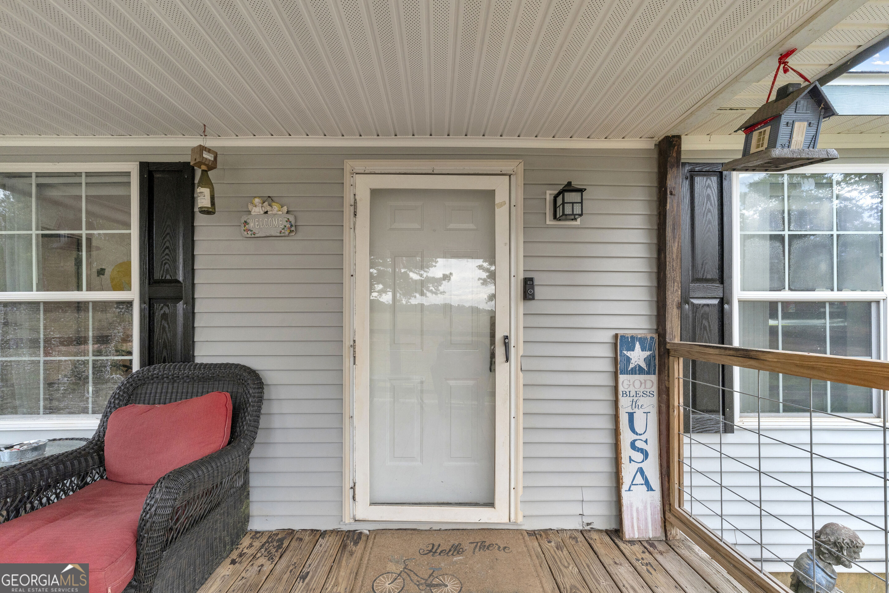 Covered front porch with a white storm door, wicker chair, and patriotic sign.