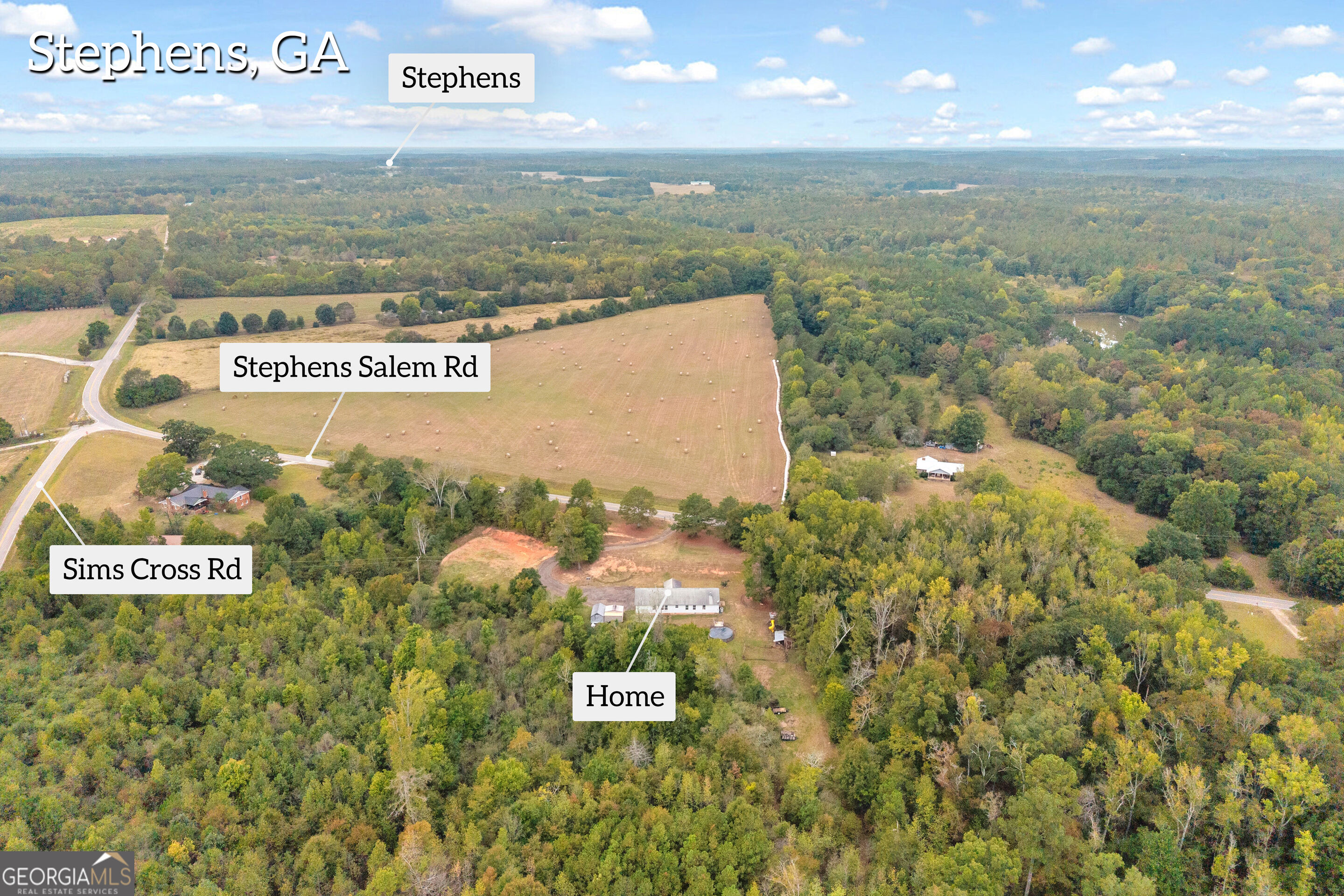 Aerial view of a home amid wooded acreage, with a neighboring hay field and roads labeled.
