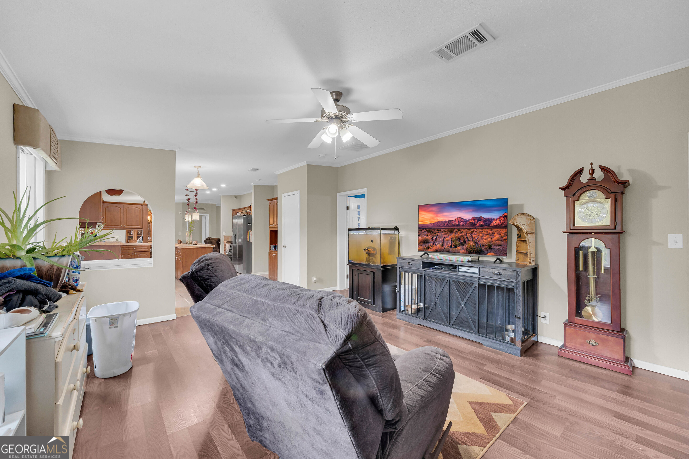Living room with a gray recliner, television, grandfather clock, and view into the kitchen.
