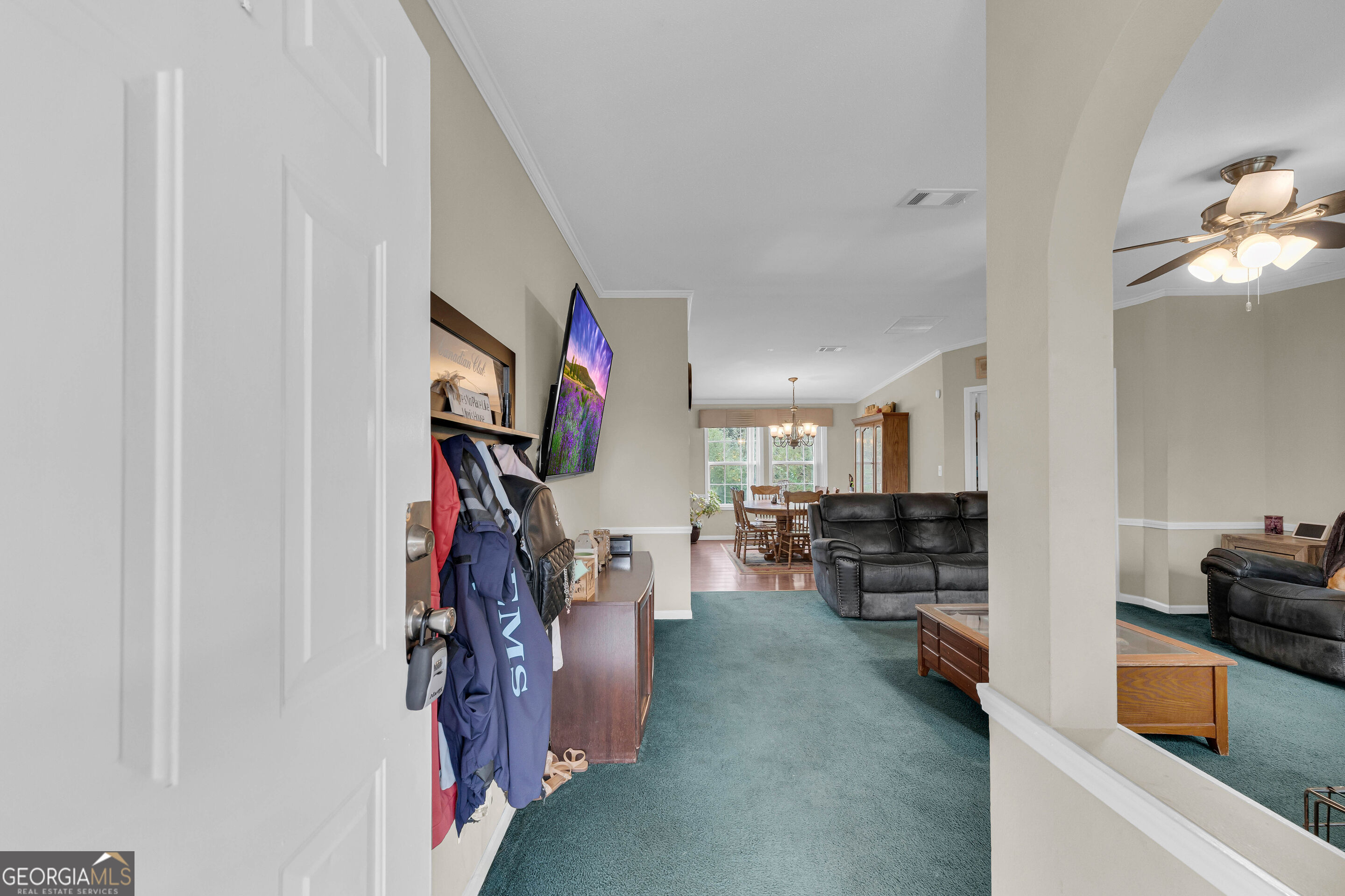 Furnished living room with teal carpet and black leather seating, opening into a dining area.
