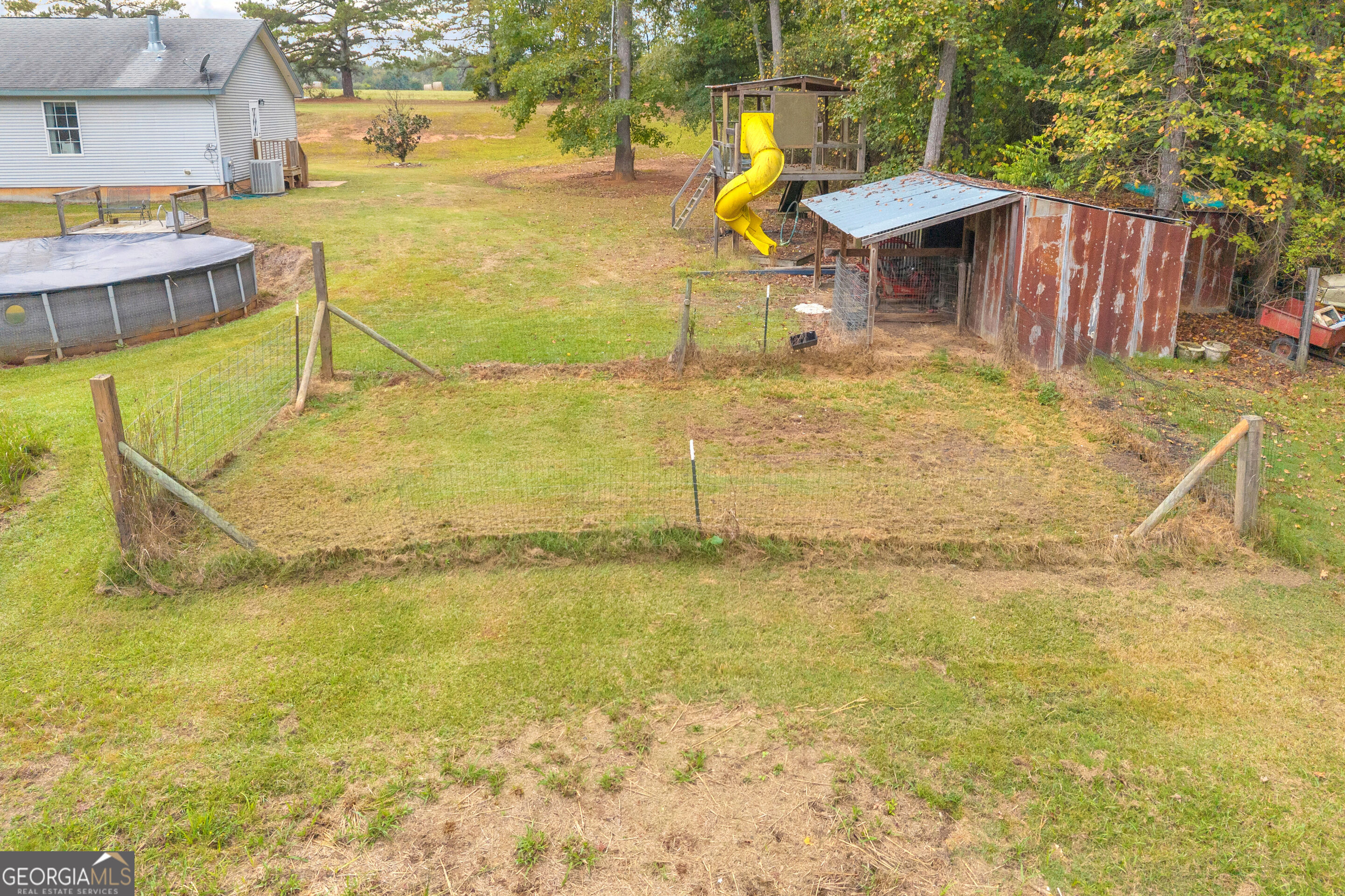 Backyard with a fenced area, above-ground pool, yellow-slide playset, and weathered shed.