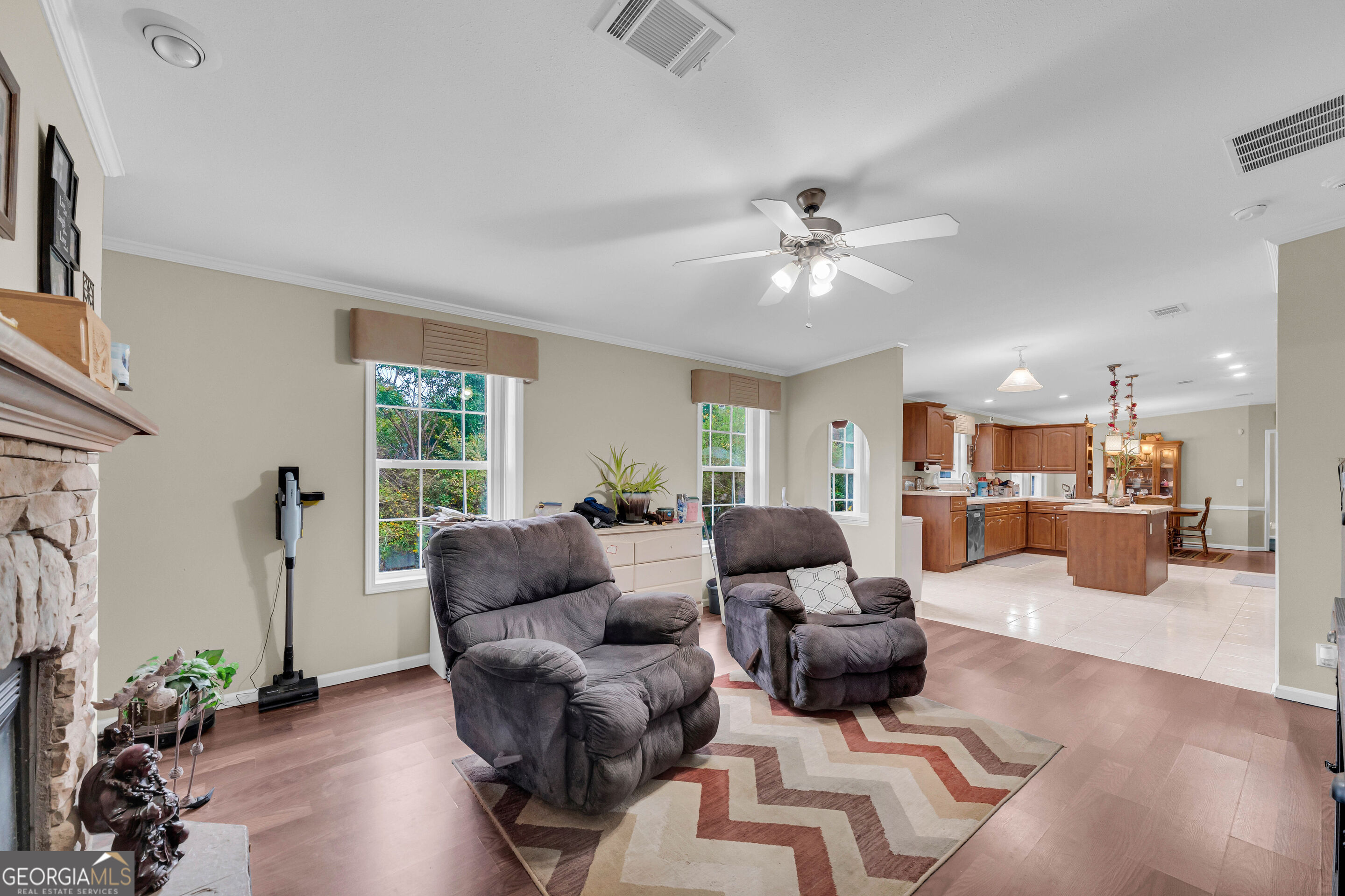 Living room with gray recliners, a stone fireplace, and an open view into the kitchen.