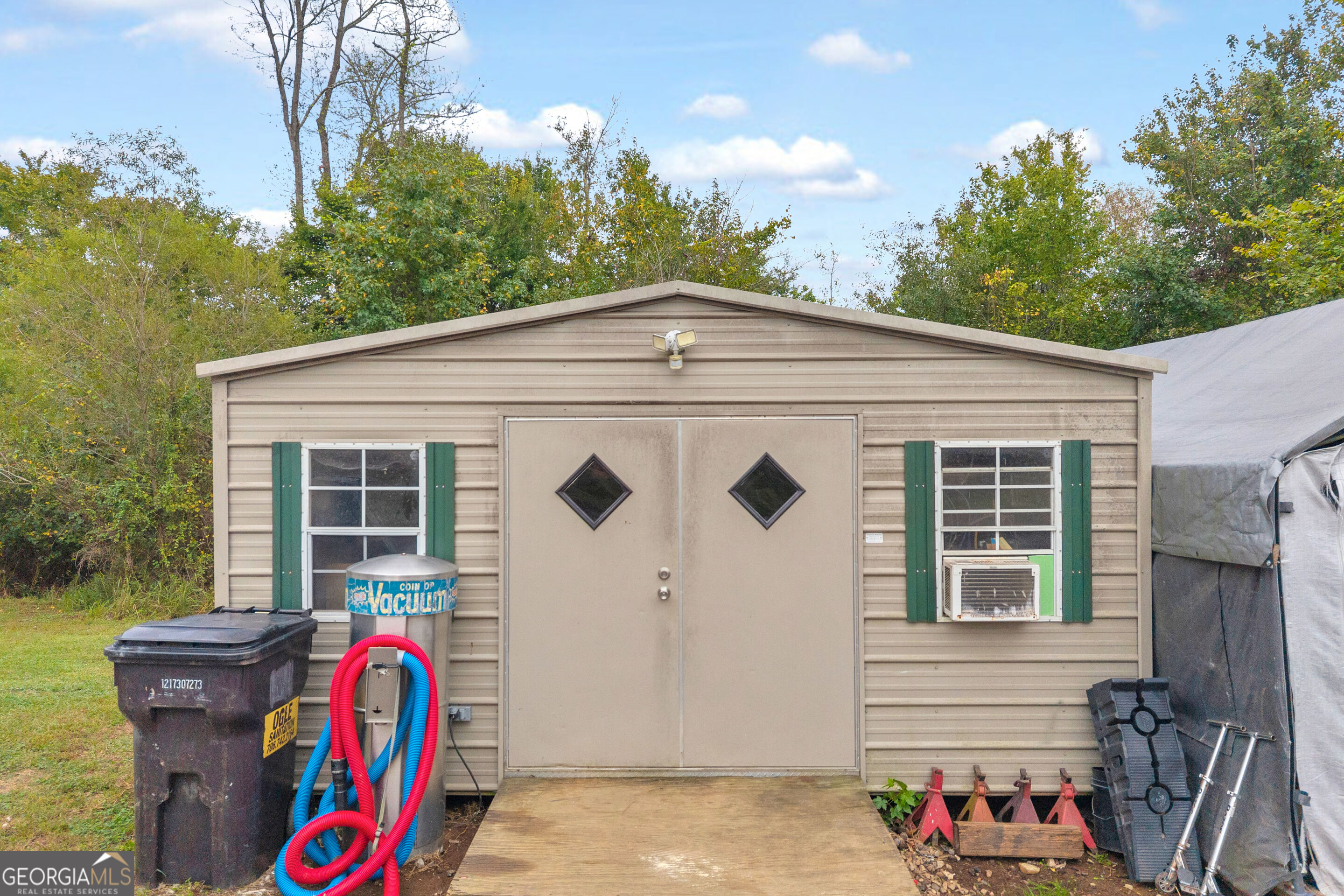 Beige-sided outbuilding with diamond-window double doors, green shutters, and equipment in front.