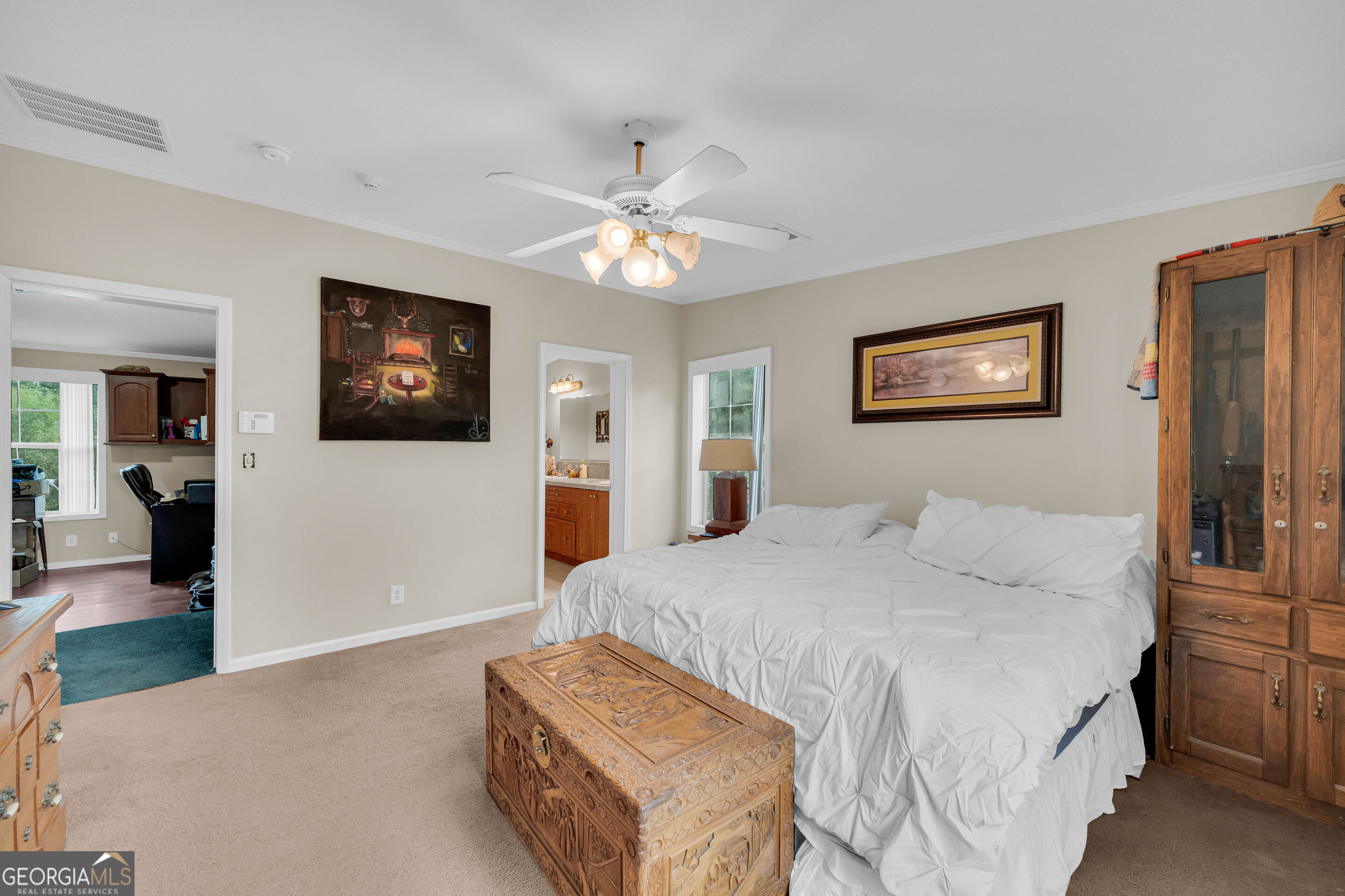 Furnished bedroom with a white bed, carved wooden chest, and glass-front cabinet.