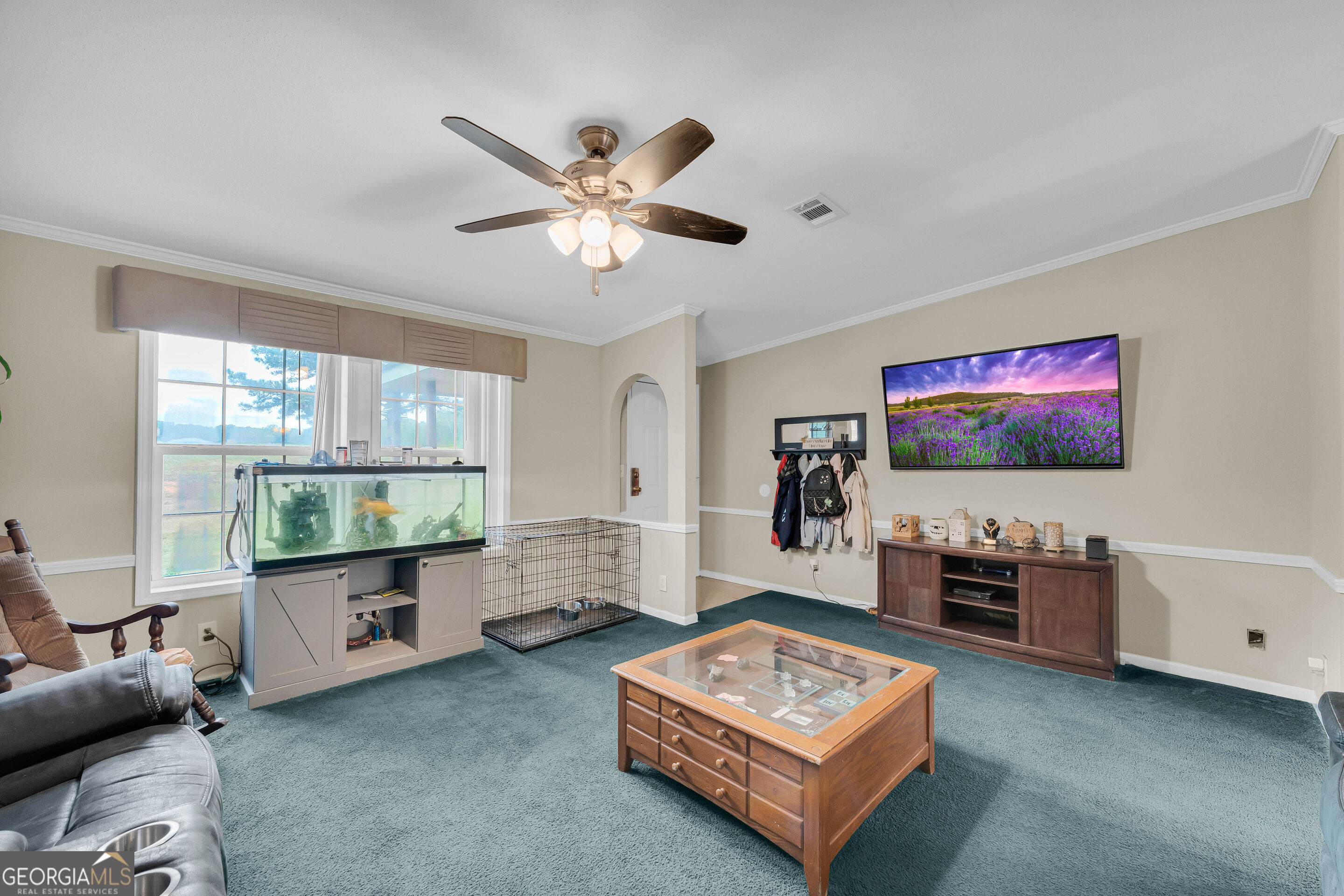 Living room with teal carpet, a large aquarium by the windows, and a wooden glass-top coffee table.