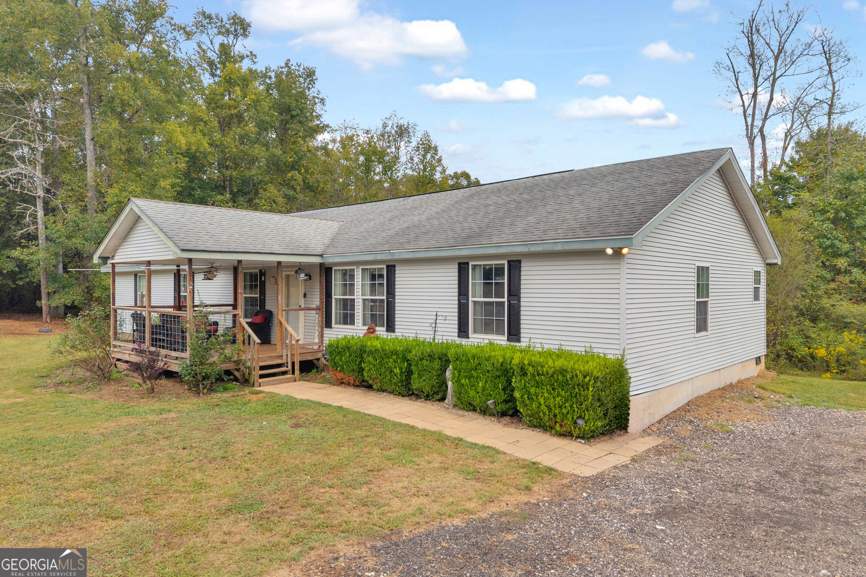 Single-story home with a covered wooden porch, front hedges, and gravel driveway.