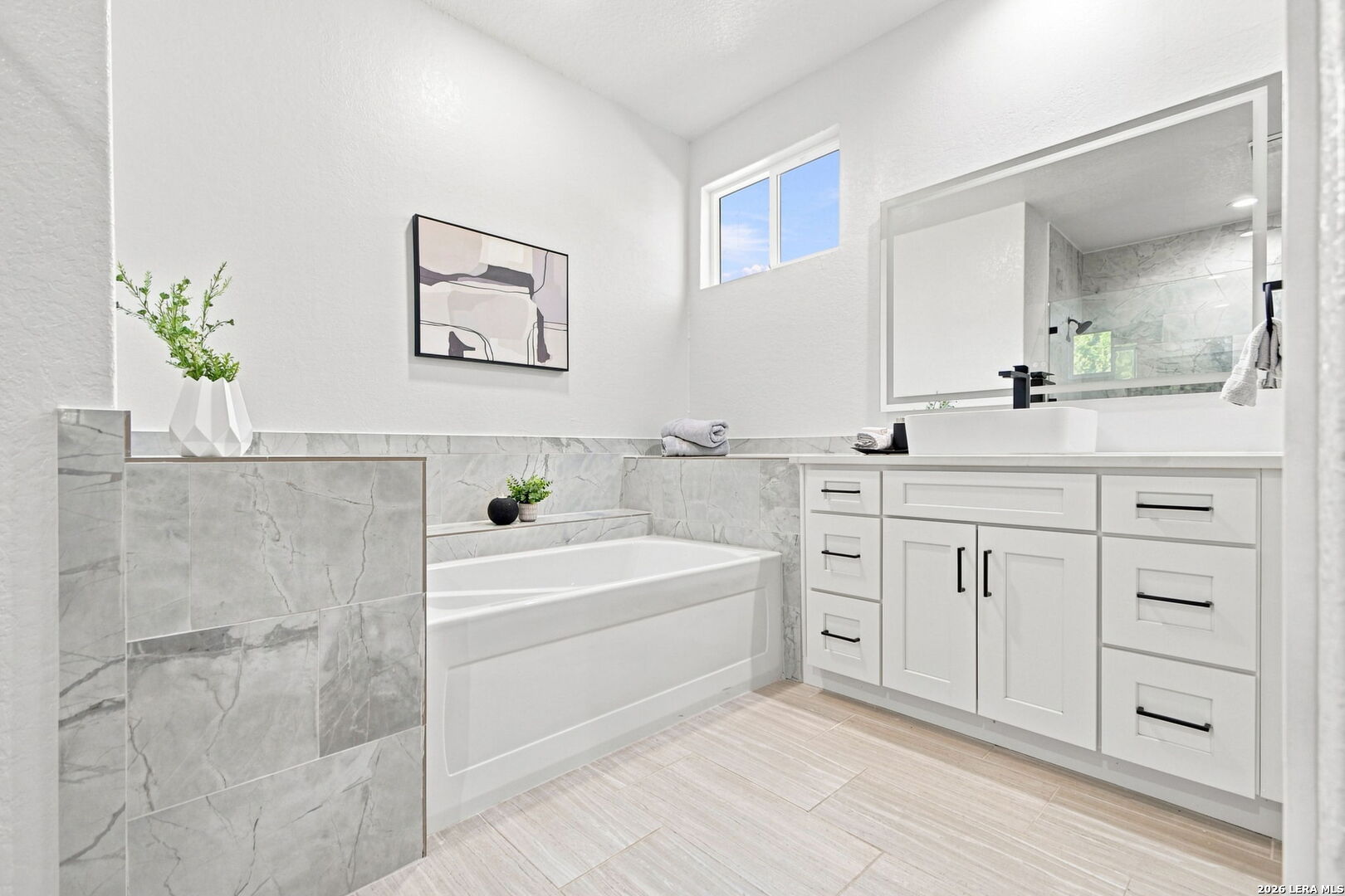 Bathroom with a white soaking tub, marble-look tile, and a white vanity with vessel sink.