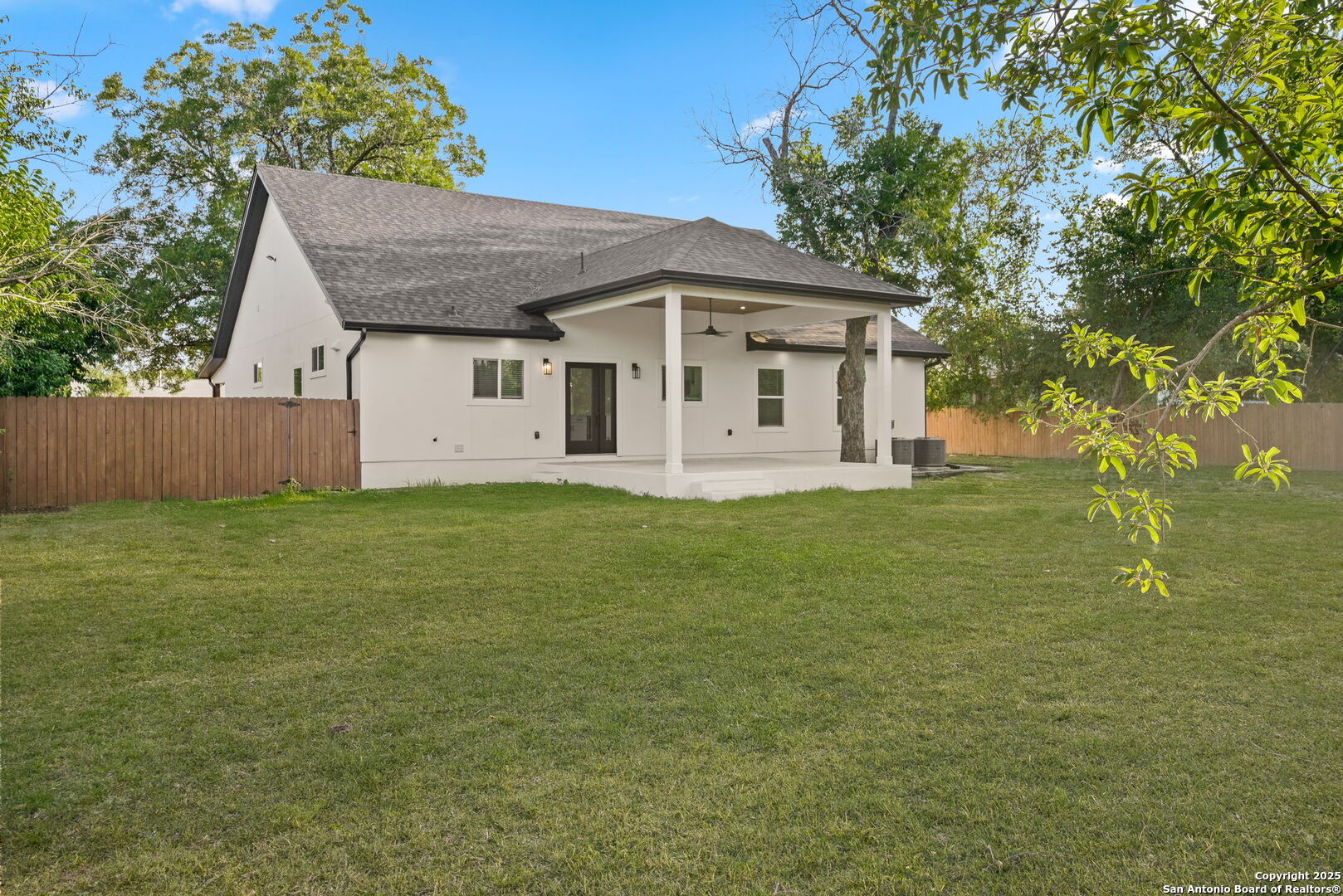 Rear exterior of a white house with a covered patio, fenced yard, and broad lawn.