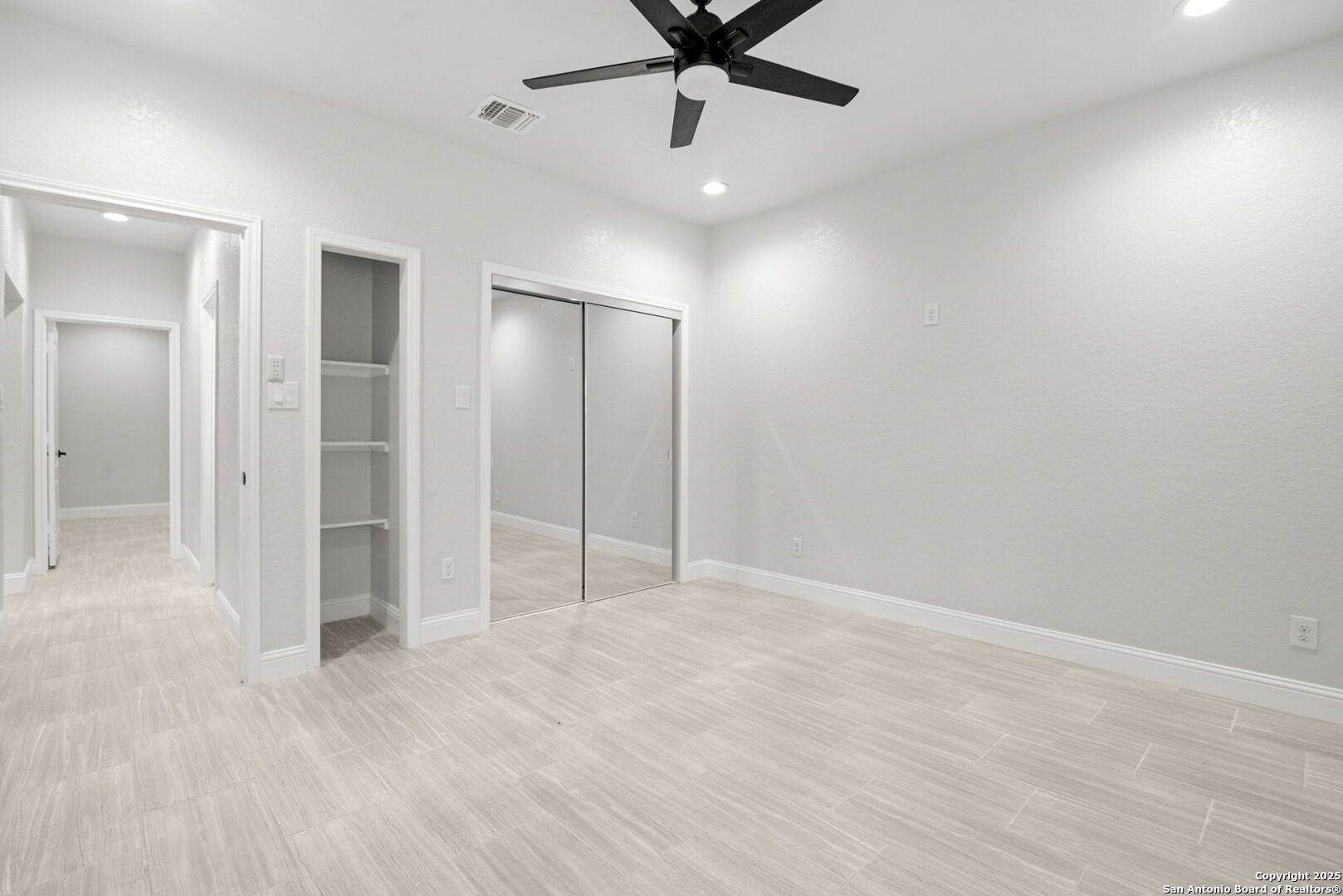 Empty bedroom with a black ceiling fan, mirrored closet doors, and light tile flooring.
