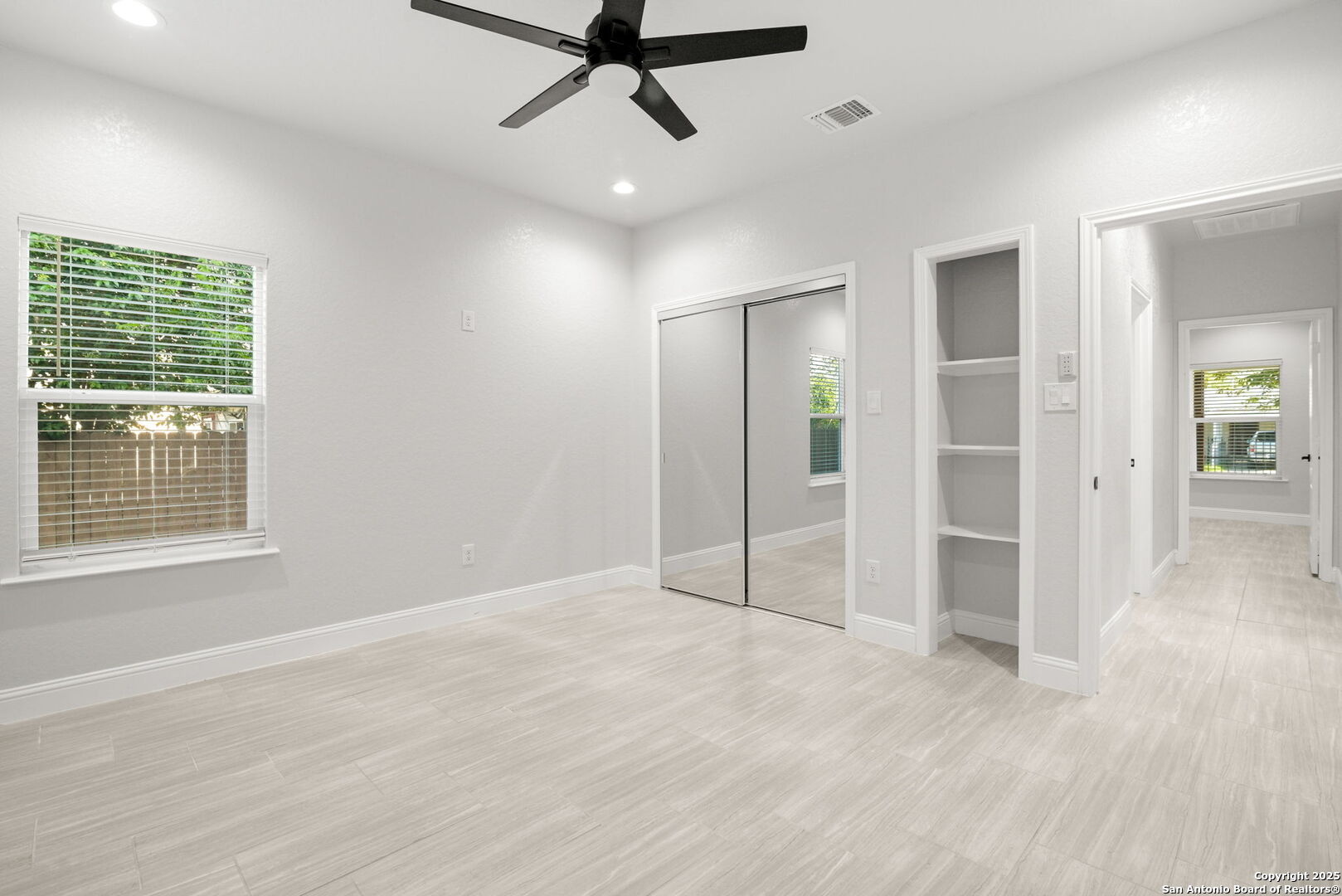 Empty bedroom with mirrored closet doors, built-in shelves, and a ceiling fan.