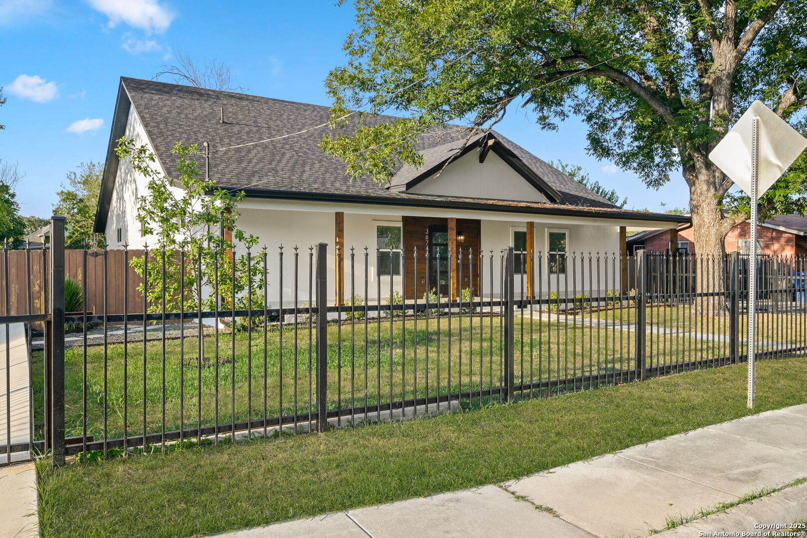 Front of a white single-story home with a dark gabled roof, wood accents, and a fenced lawn.