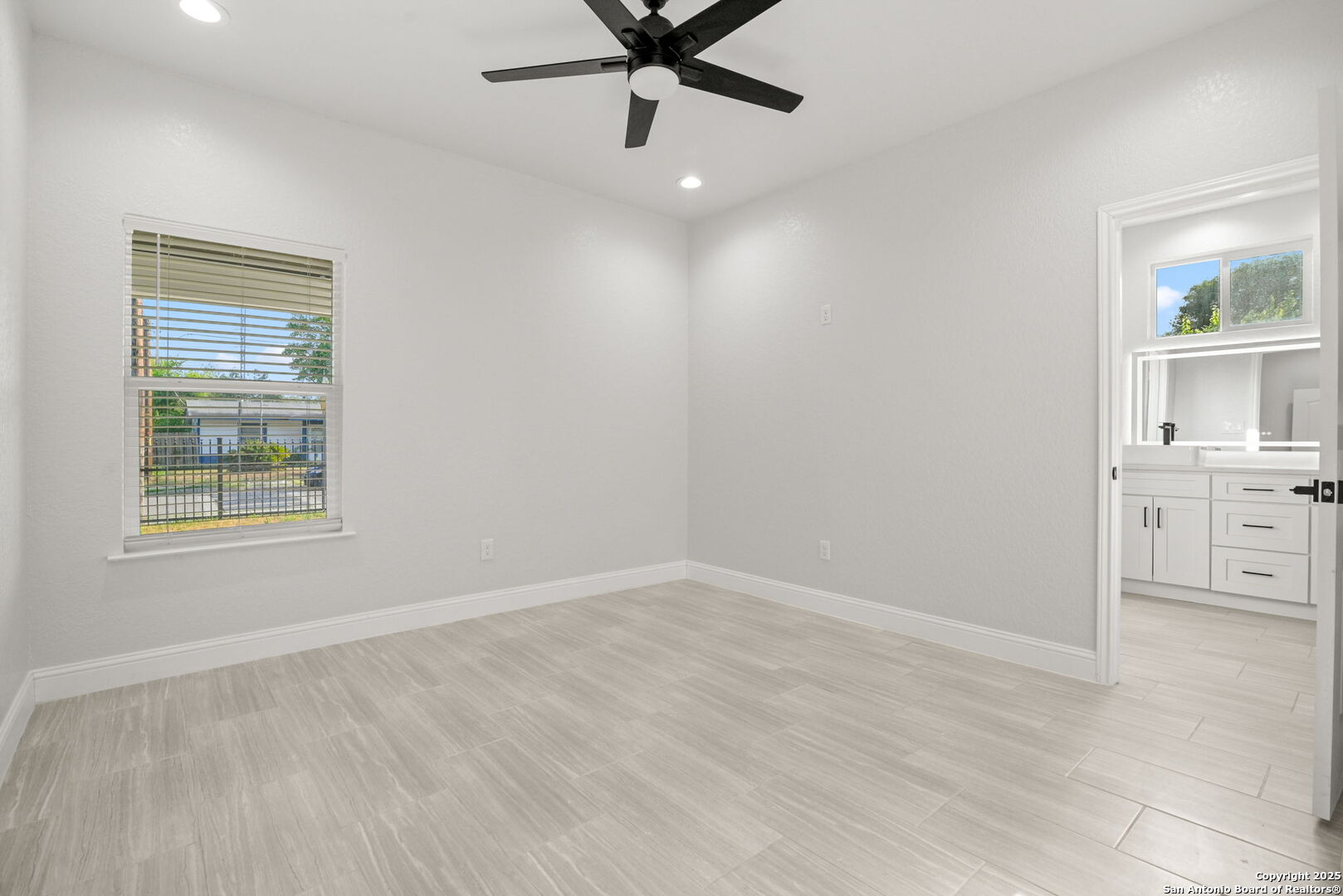 Empty room with light tile flooring, a black ceiling fan, and an adjoining bathroom vanity.