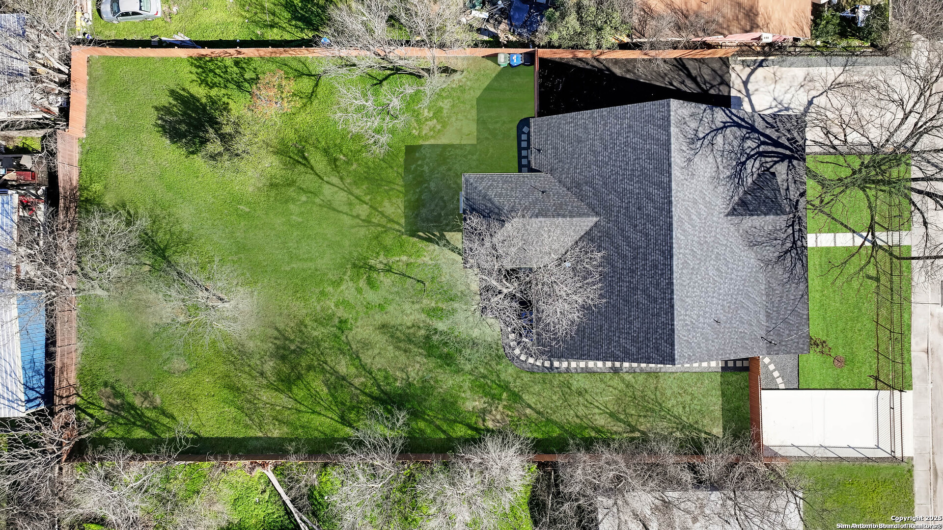 Aerial view of a home with a large fenced lawn and driveway.