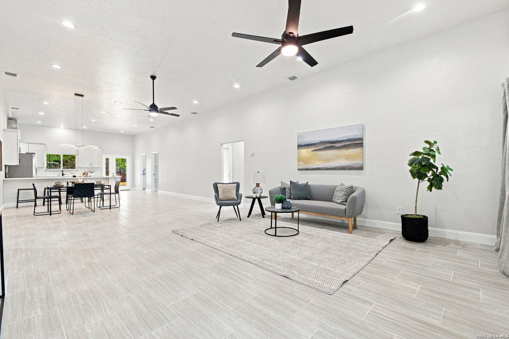 Open-plan living room with gray sofa, tiled floors, and adjoining dining area and kitchen.