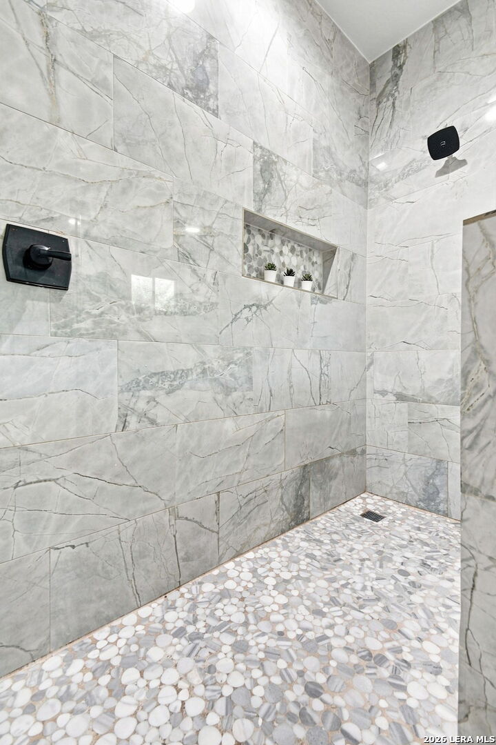 Walk-in shower with marble-look walls, a pebble floor, and a recessed niche with plants.
