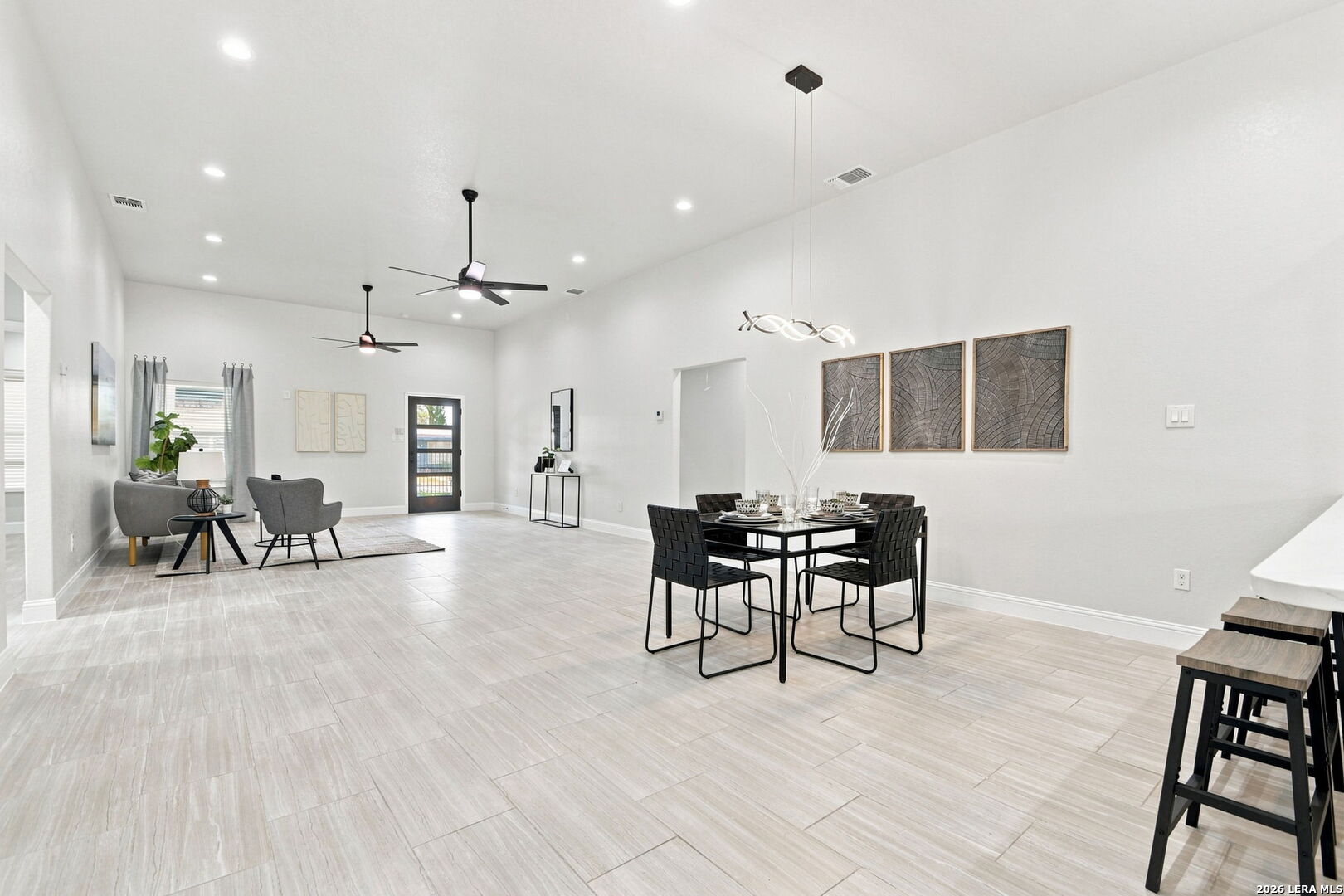 Open-plan living and dining area with gray seating, tiled floors, and modern pendant lighting.