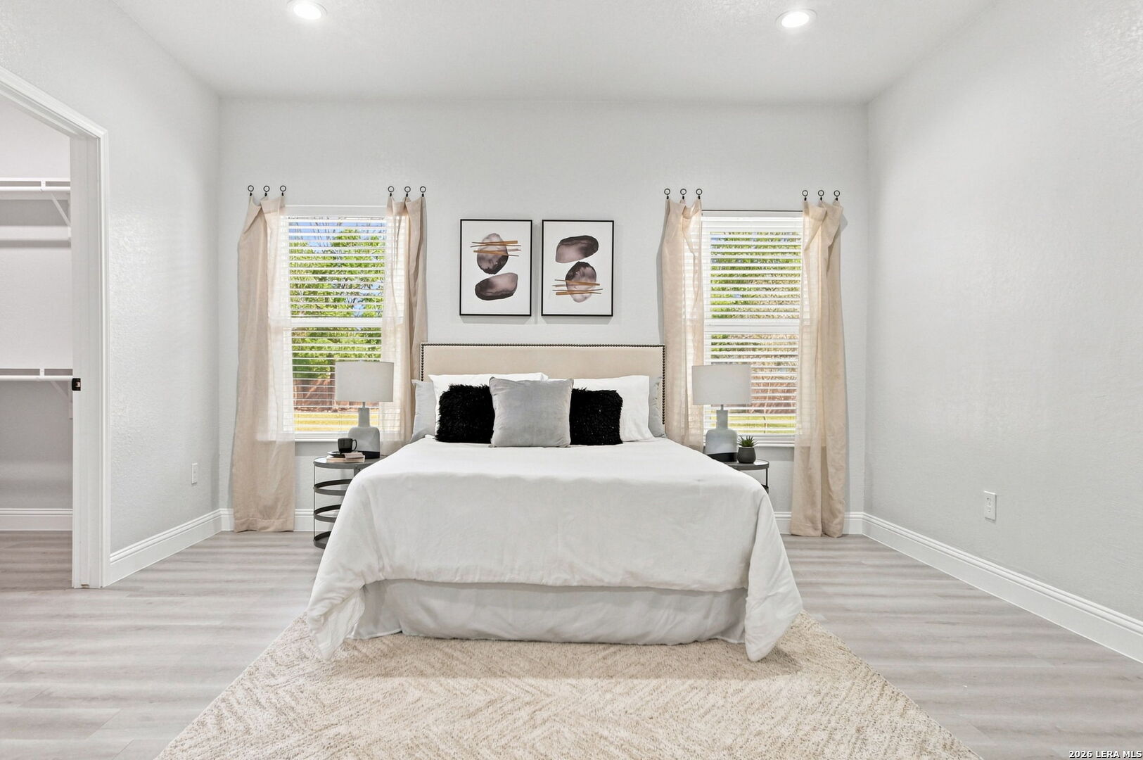 Staged bedroom with a centered white bed between two curtained windows.